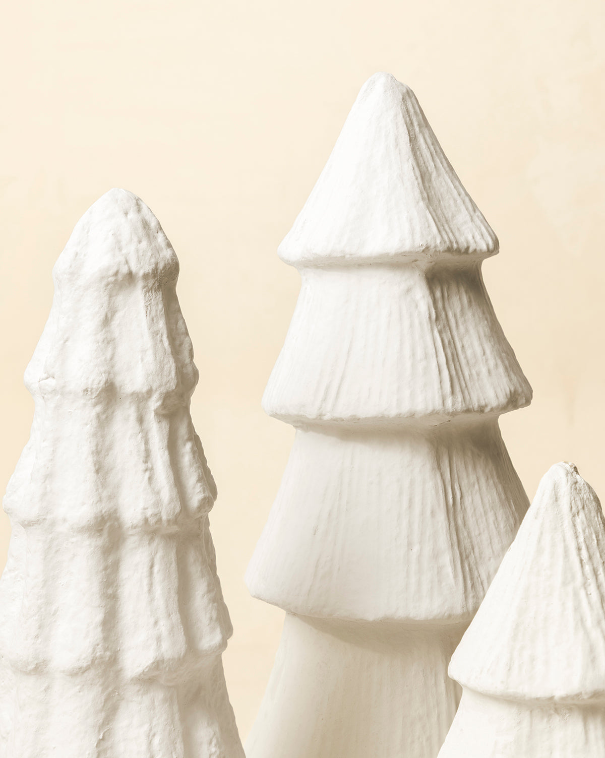 Three white, textured Confectioners Paper Mache Trees with a cone shape are grouped together against a beige background, creating a perfect handcrafted holiday décor accent, by Vendixs
