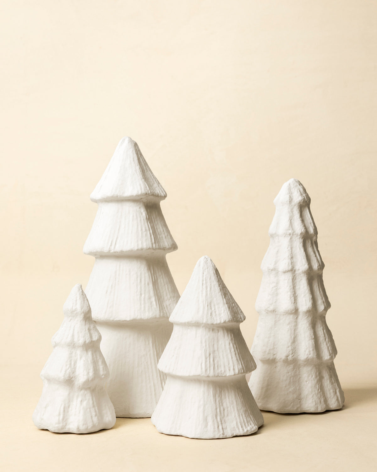 Four white, textured Confectioners Paper Mache Trees of varying heights stand closely together on a neutral background, creating a minimalist, winter-themed holiday décor display, by Vendixs