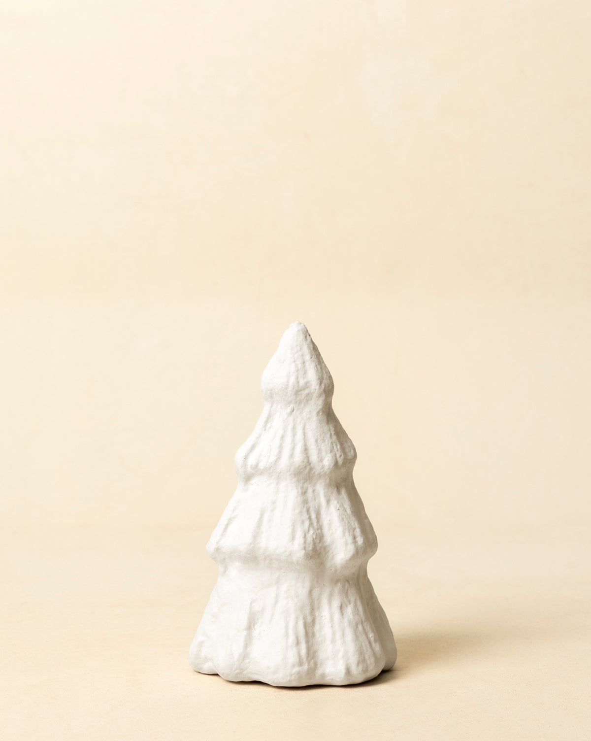 The Confectioners Paper Mache Tree, a small white handcrafted ornament with a textured surface, sits on a light beige background—perfect for holiday décor, by Vendixs