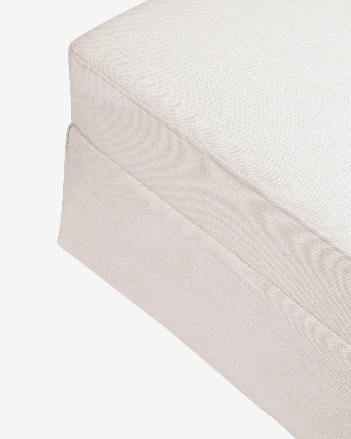 Close-up of the corner of a light beige Million Dollar Baby Crawford Gliding Ottoman with eco-performance upholstery and a tailored skirt, shown on a white background, Vendixs