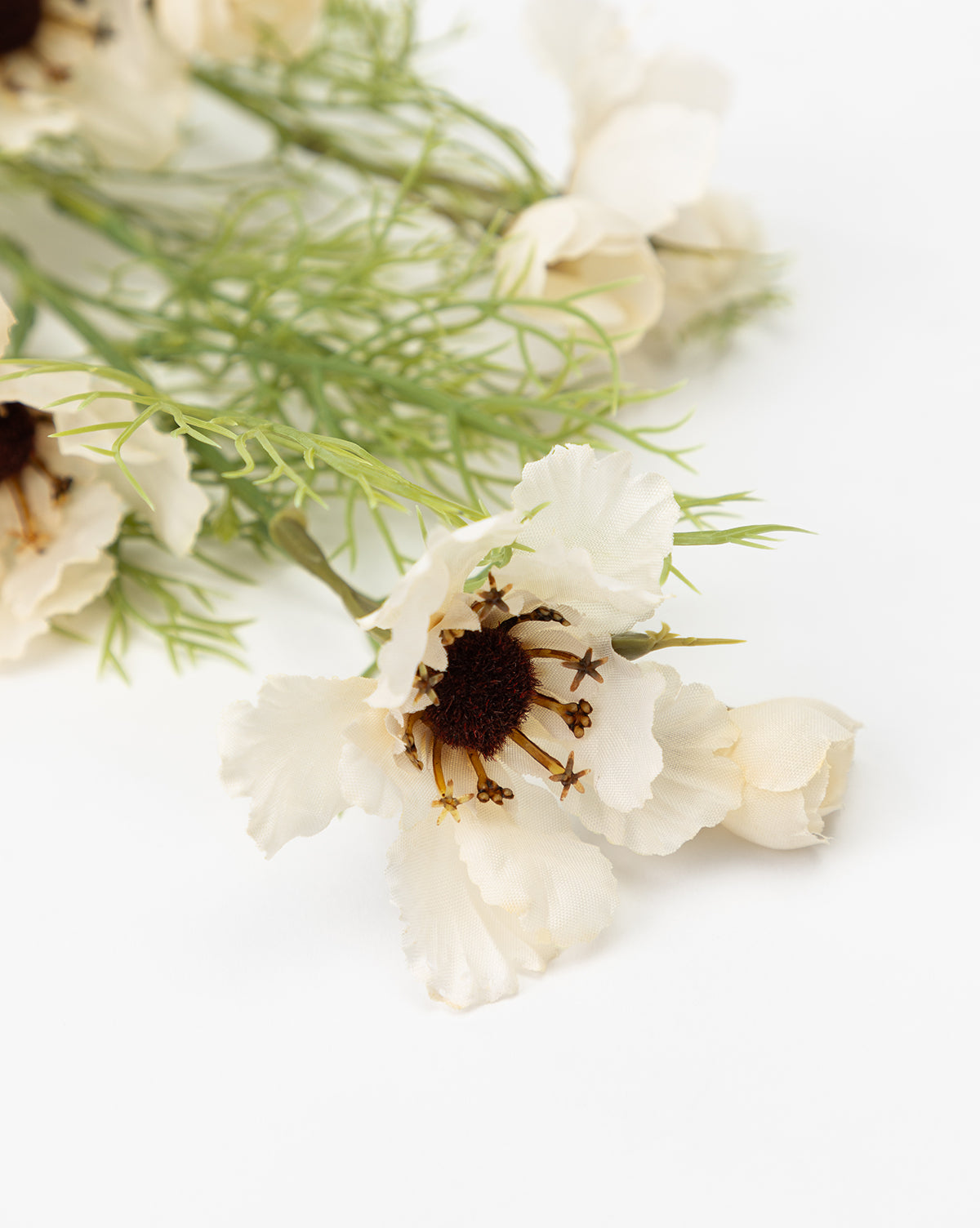 A close-up of the Cream Cosmos Stem showcases white artificial flowers with dark brown centers and green leaves, artfully arranged as a faux floral display against a white background, by Vendixs