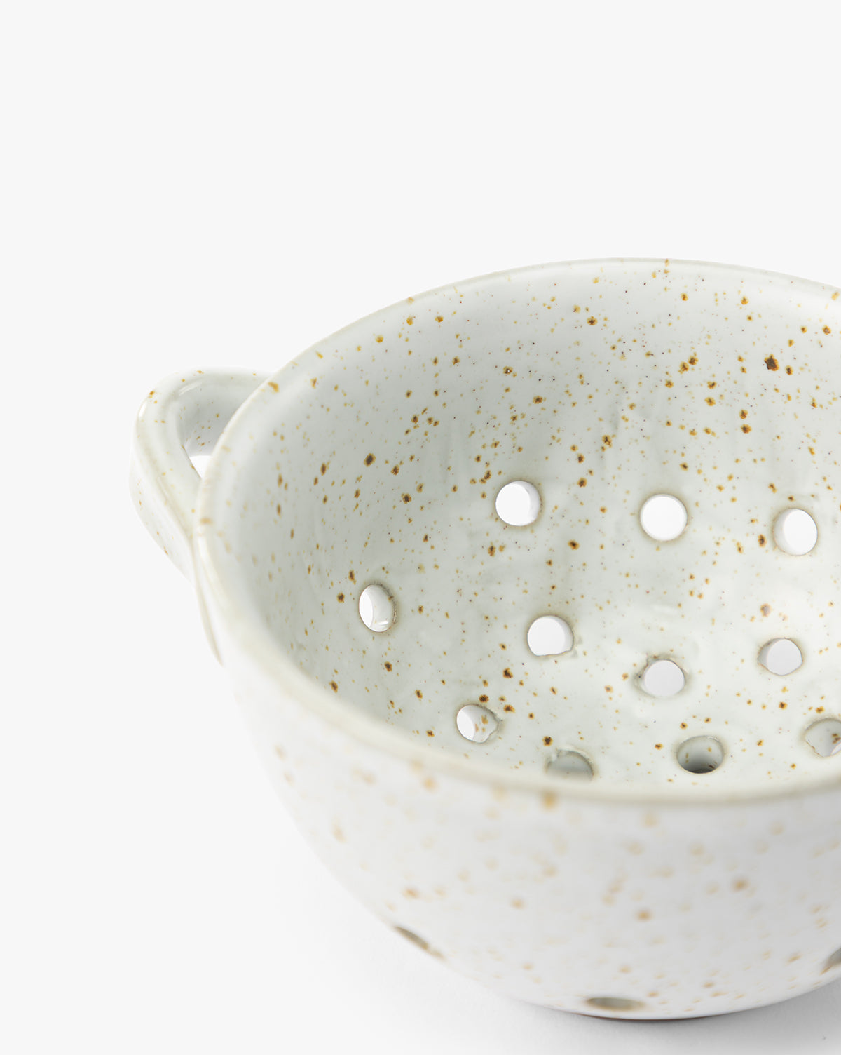 A close-up of the Cream Handled Berry Bowl, an artisanal stoneware piece with a small handle and multiple round holes in the bottom, set against a white background, by Vendixs