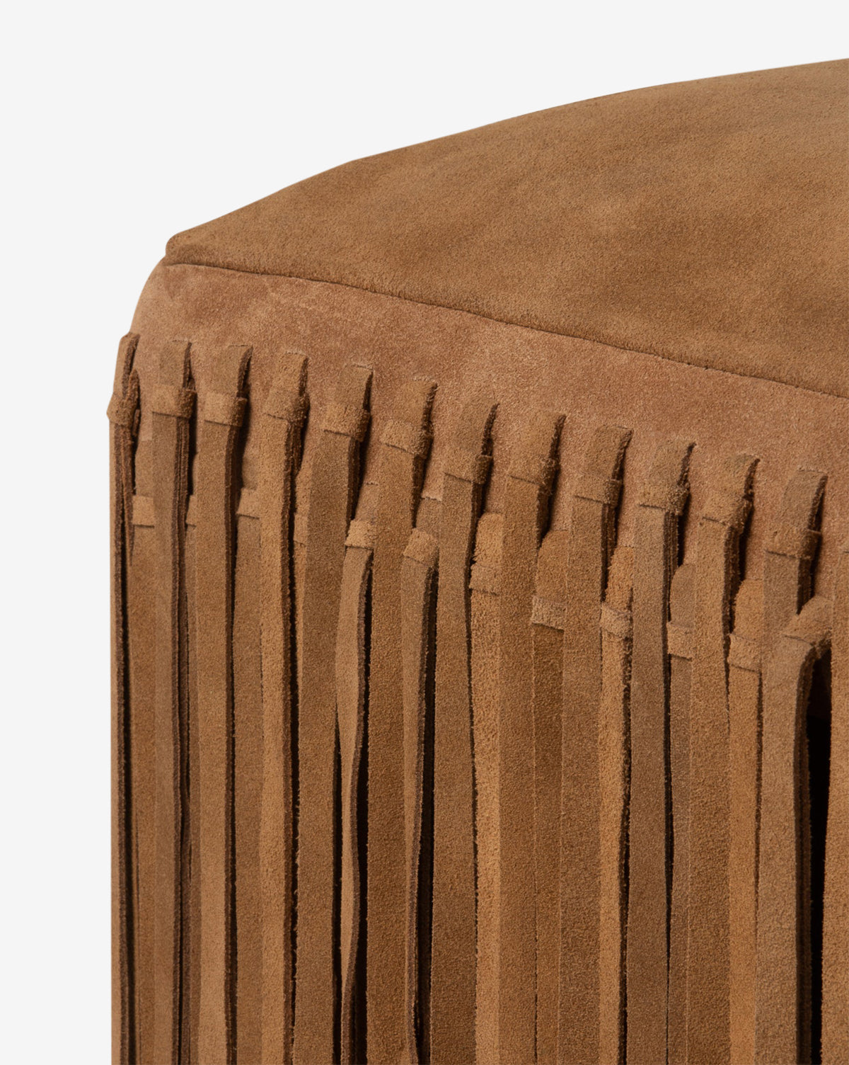 The Damian Ottoman by Made Goods is shown in a rich camel suede with long fringe detailing along the side, set against a white background. Vendixs