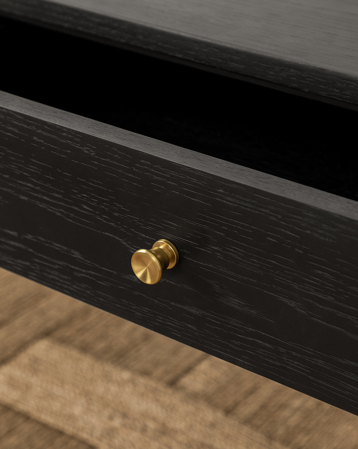 A close-up of an open black wooden drawer with a round gold knob from the Dana 2-Drawer Console, set on a textured light brown floor—ideal for adding style to your entryway, by Vendixs