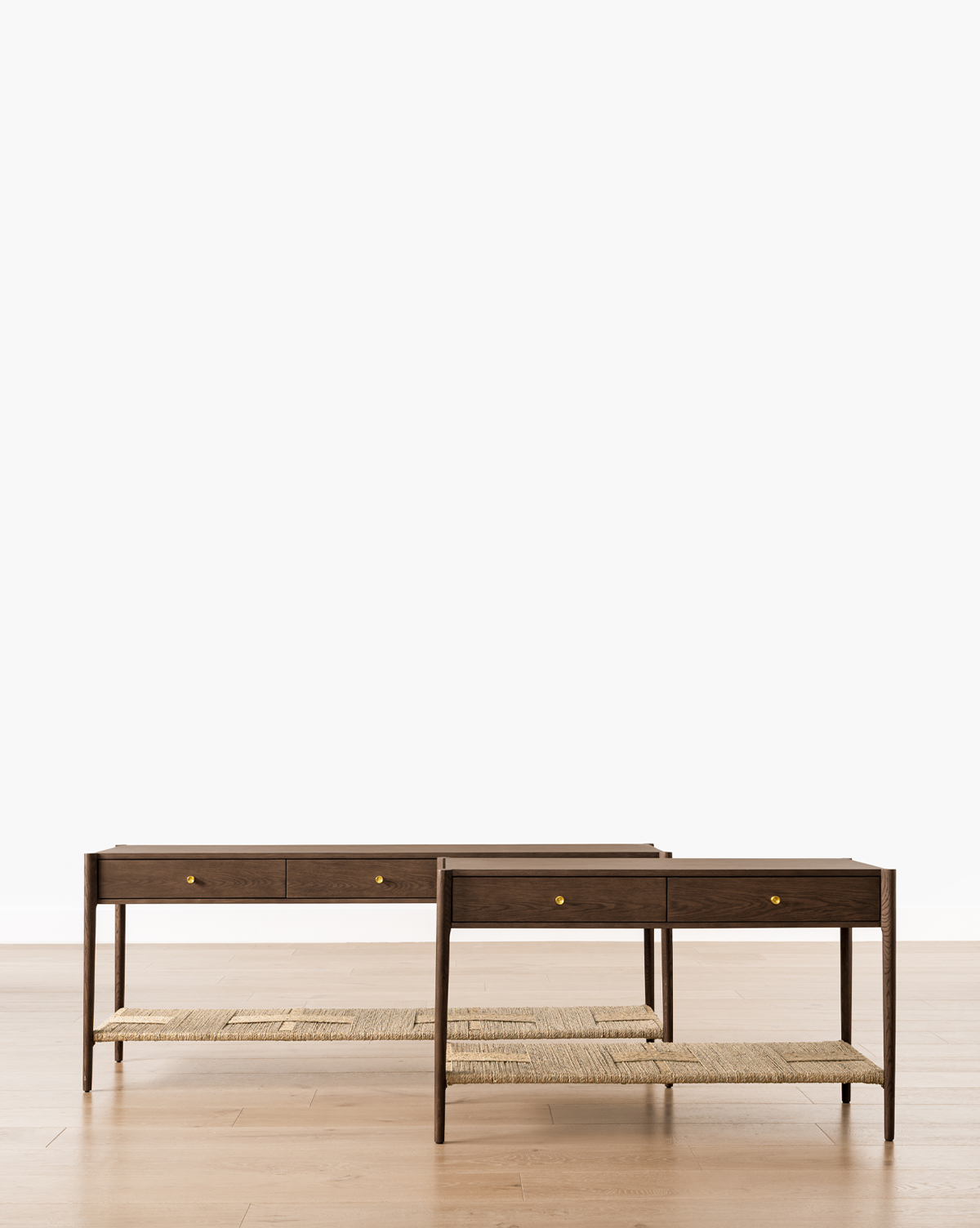 Two Dana Walnut Oak Console tables with woven shelves, small drawers, and brass hardware are placed side by side on a light wood floor against a plain white background, by Vendixs
