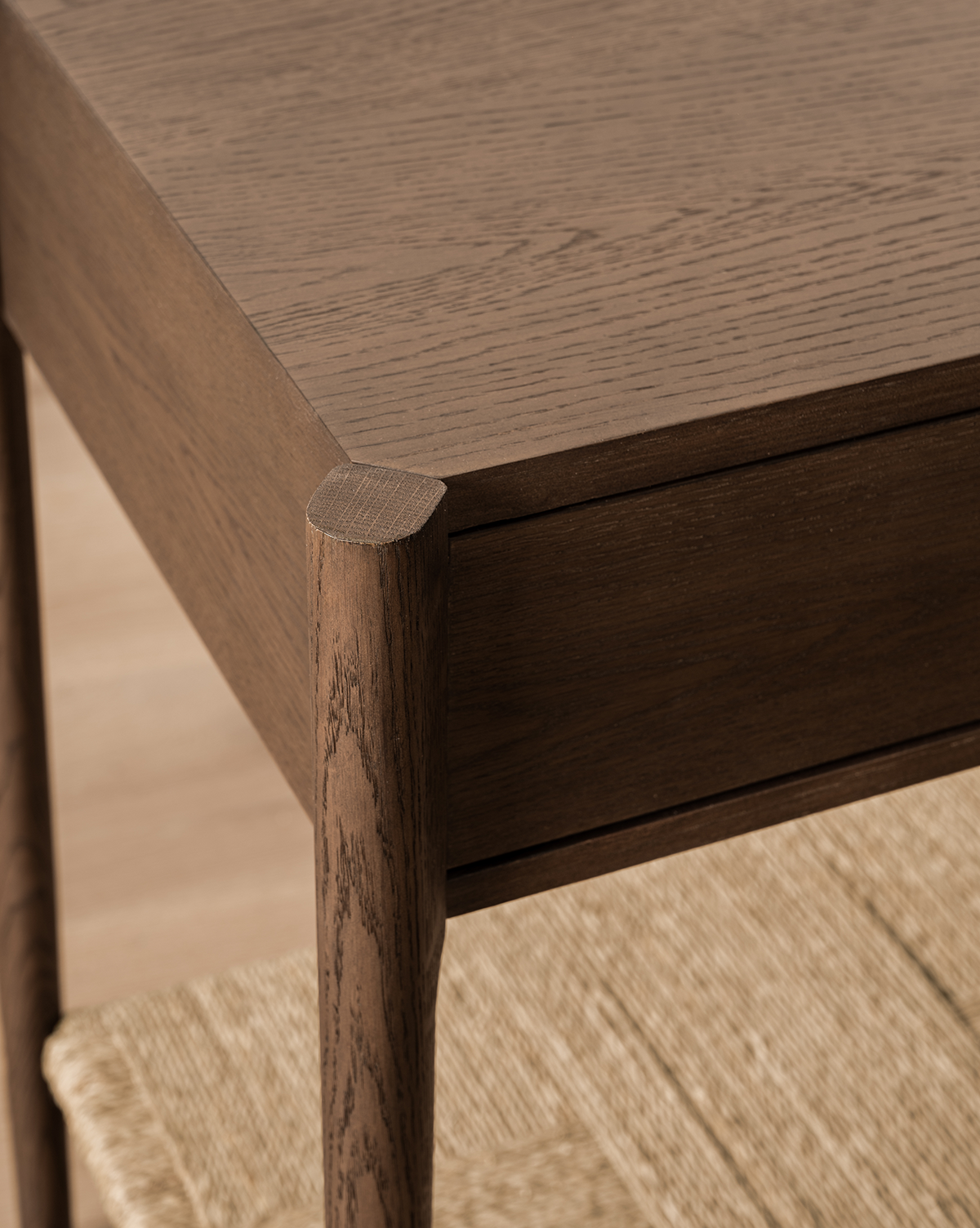 Close-up of the Dana Walnut Oak Console’s corner, featuring rounded legs, a smooth dark finish, and a partially visible woven shelf beneath, by Vendixs