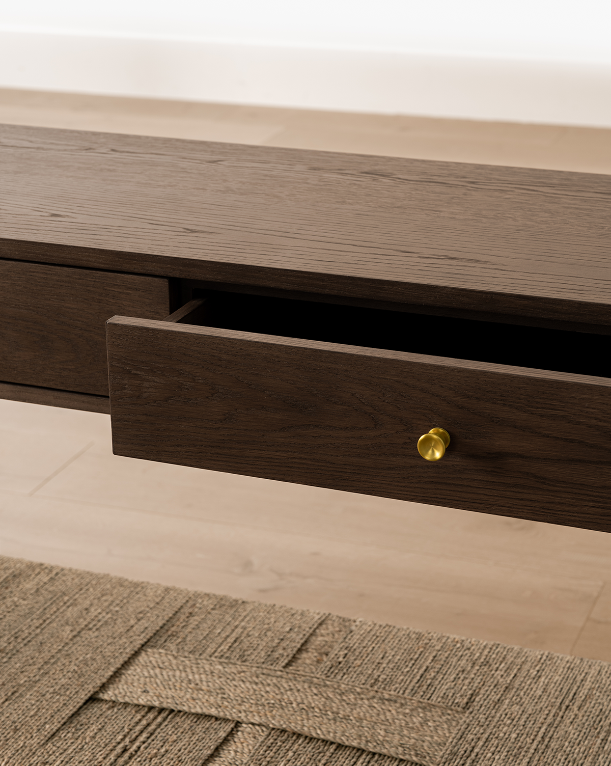 A close-up of the Dana Walnut Oak Console with an open drawer and brass knob, set on a light wood floor beside a textured beige rug, by Vendixs