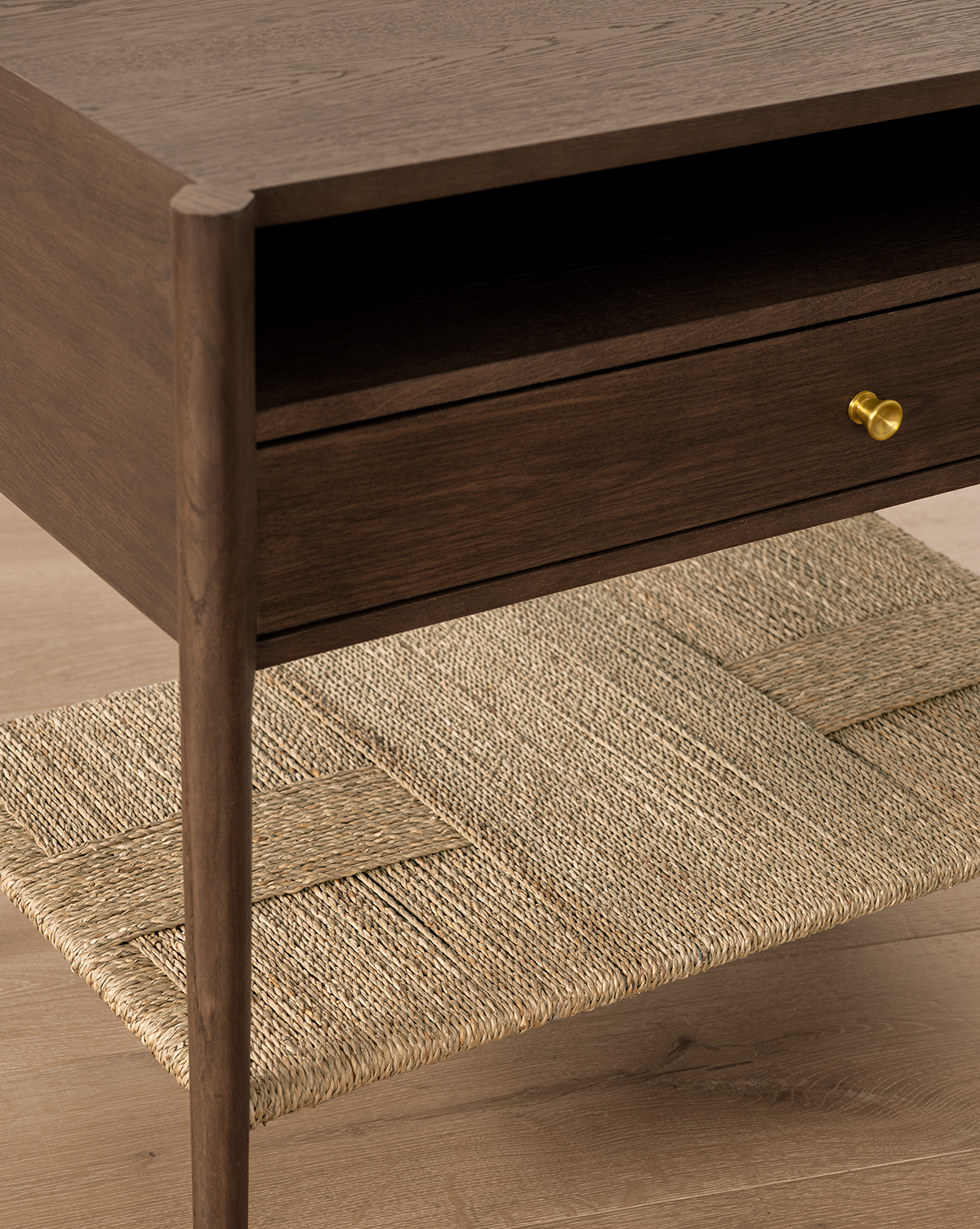 A close-up of the Dana Walnut Oak Nightstand featuring a drawer with brass hardware and an open rattan shelf, set on a light wood floor, by Vendixs