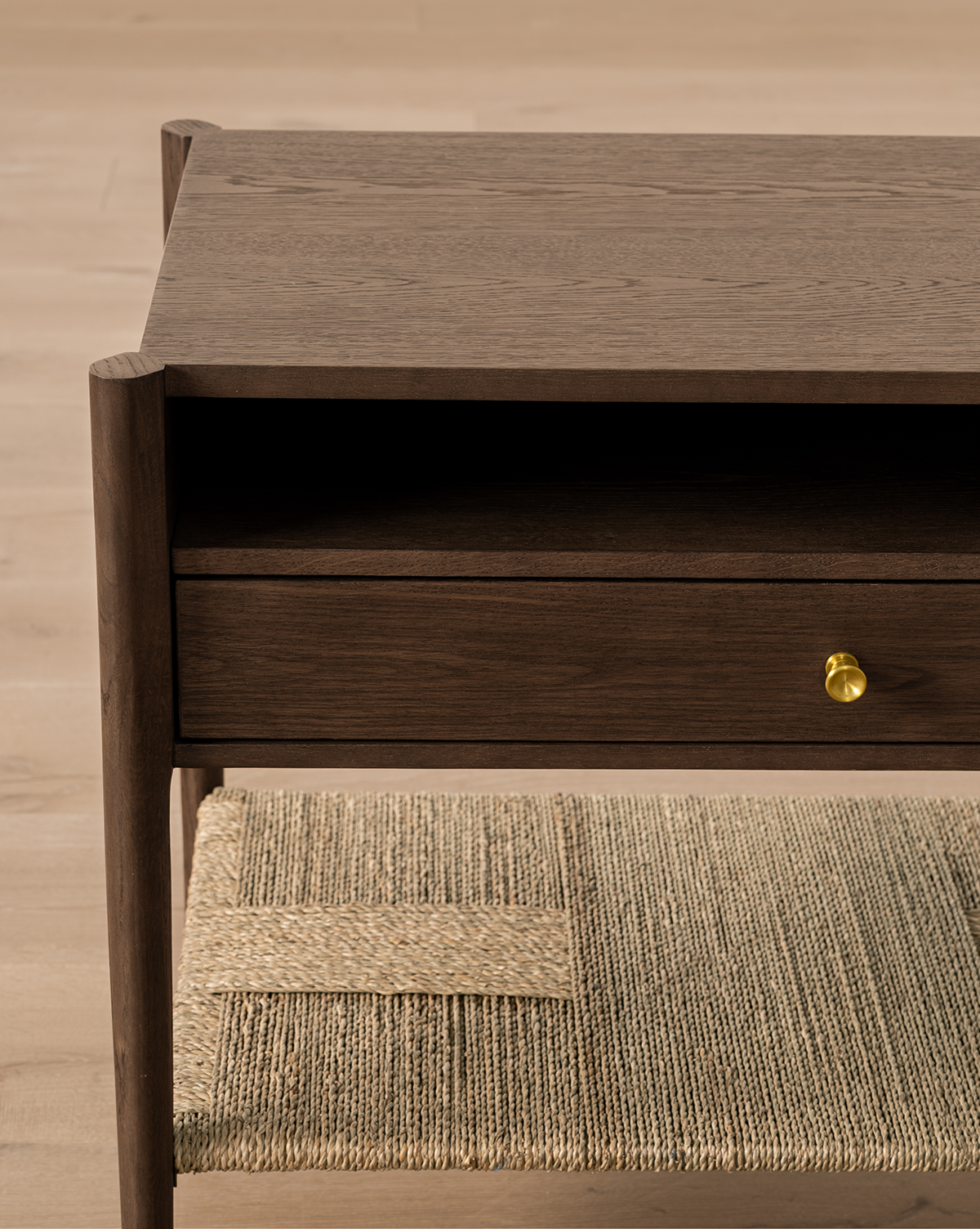 The Dana Walnut Oak Nightstand features a single drawer with a round brass knob, an open shelf above, and a woven rattan lower shelf, all set on a light wood floor, by Vendixs