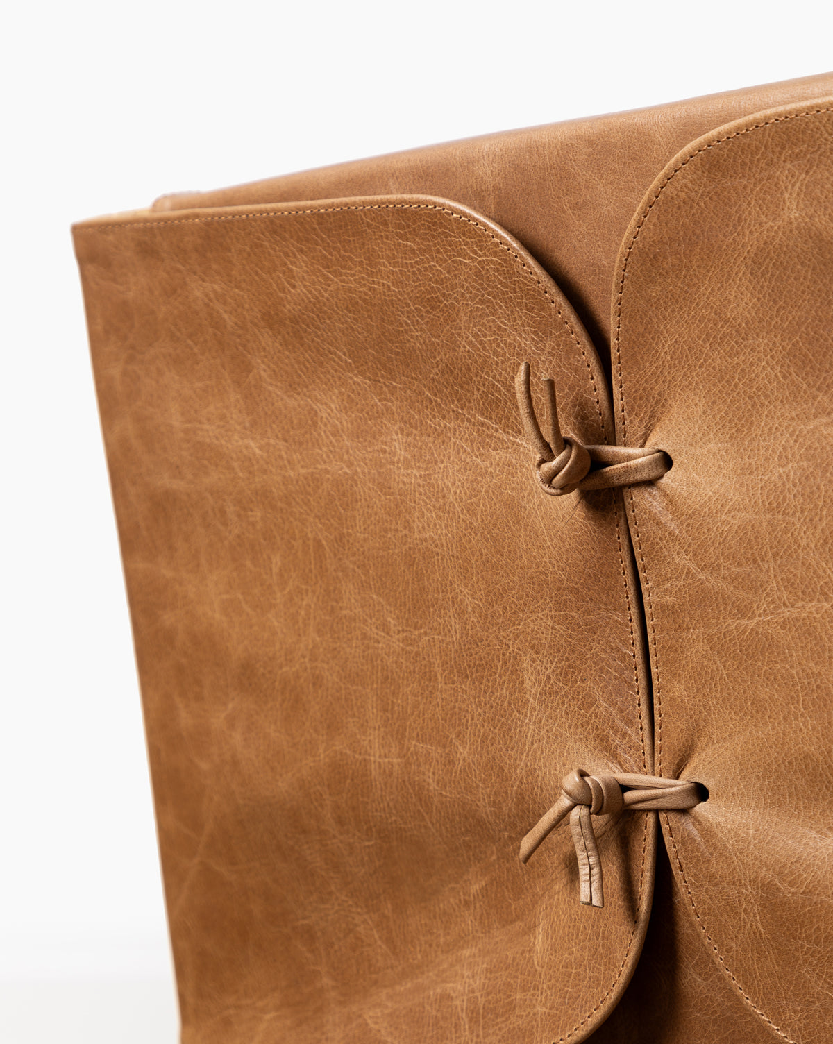 Close-up of the Danson Dining Chair with a light brown leather seat featuring a textured surface and minimalist design. Two leather straps tied in knots secure the flap, while a plain white background highlights its expert craftsmanship, by Vendixs