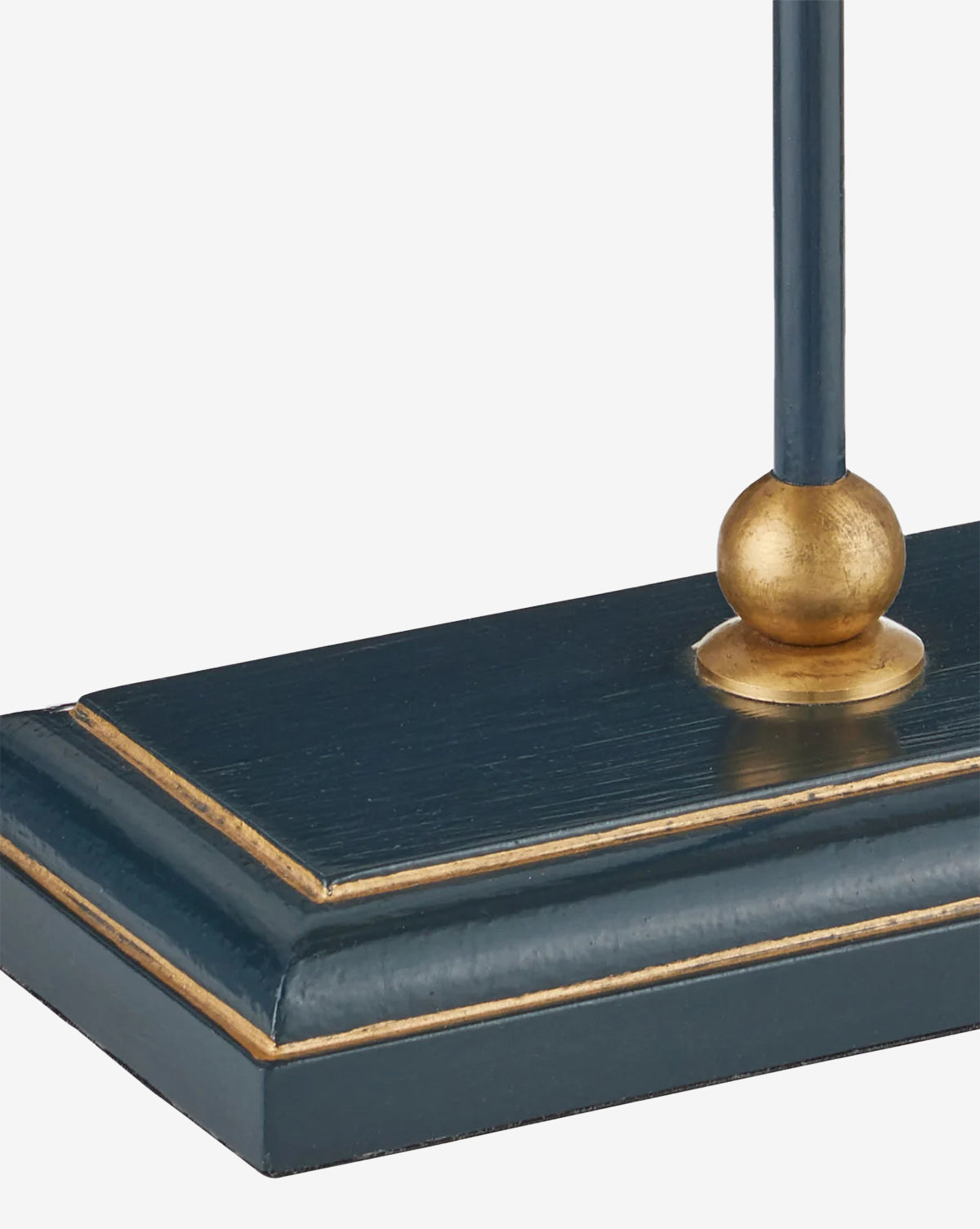 A close-up of the Daphne Navy Table Lamp, showcasing its dark blue rectangular base with gold accents and a gold sphere where the stem connects to the base, by Vendixs