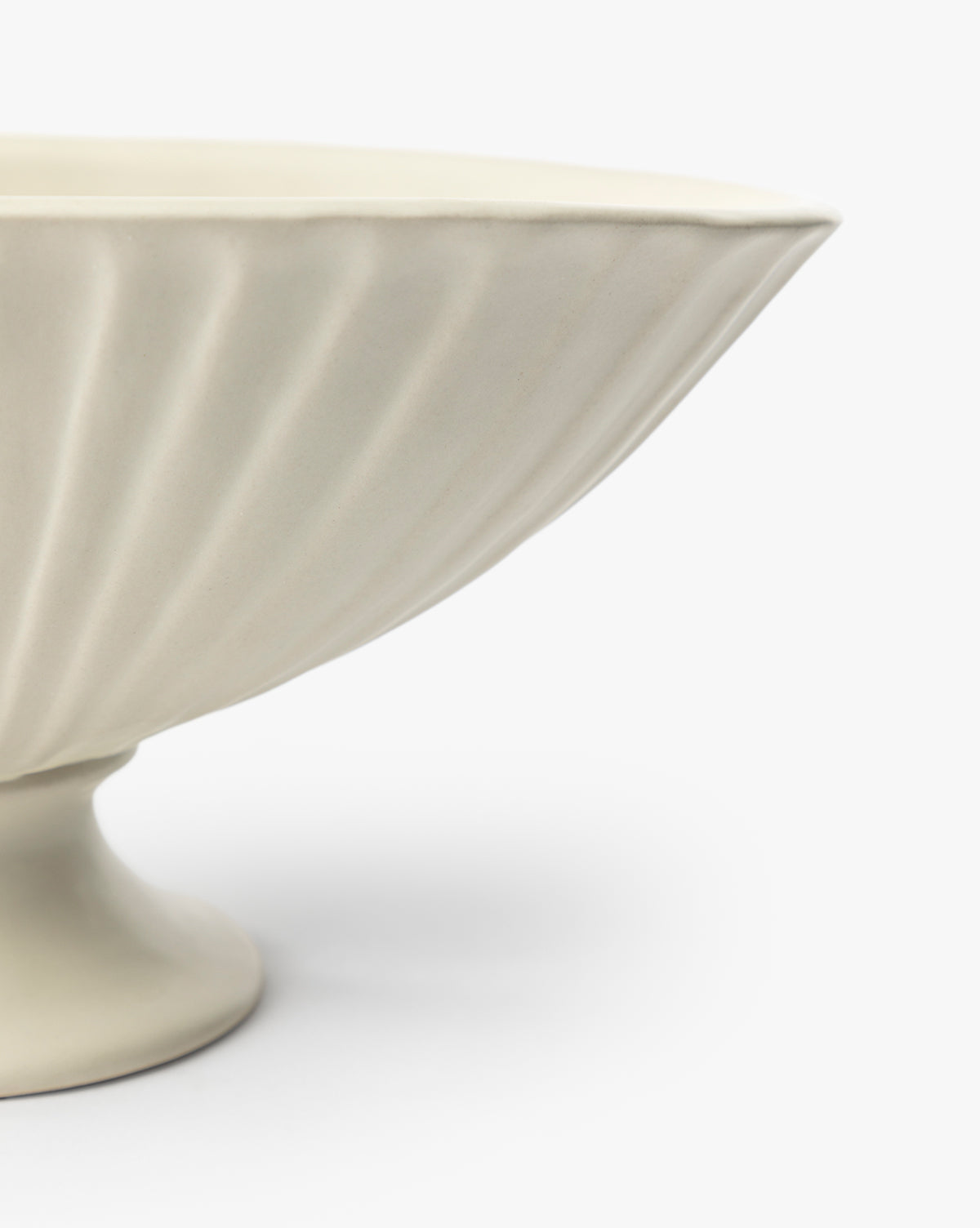 A close-up of the Delphi Footed Bowl, featuring cream-colored stoneware with a fluted textured design and satin glaze, shown against a plain white background, by Vendixs