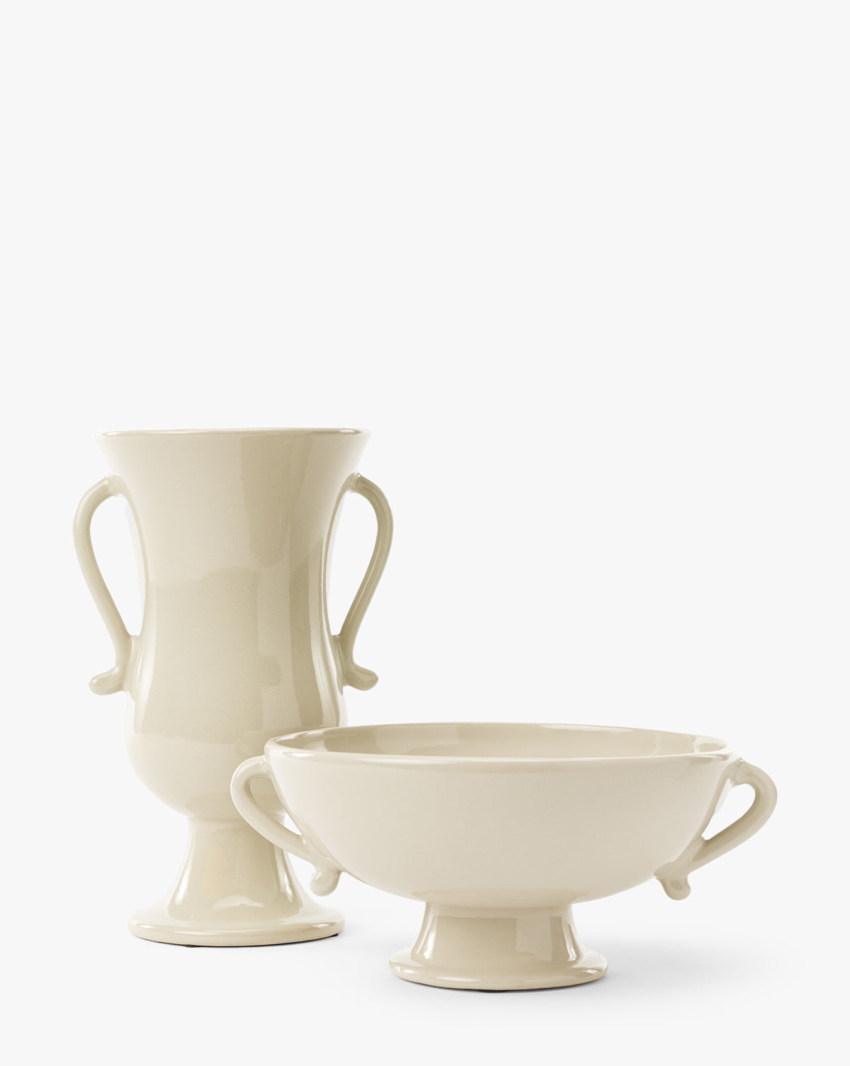 The Delphine Footed Bowl is a cream-colored ceramic vase with a glossy finish, side handles, and a pedestal base. Its bowl shape and elegant design make it perfect for displaying flowers or as a decorative accent by Vendixs