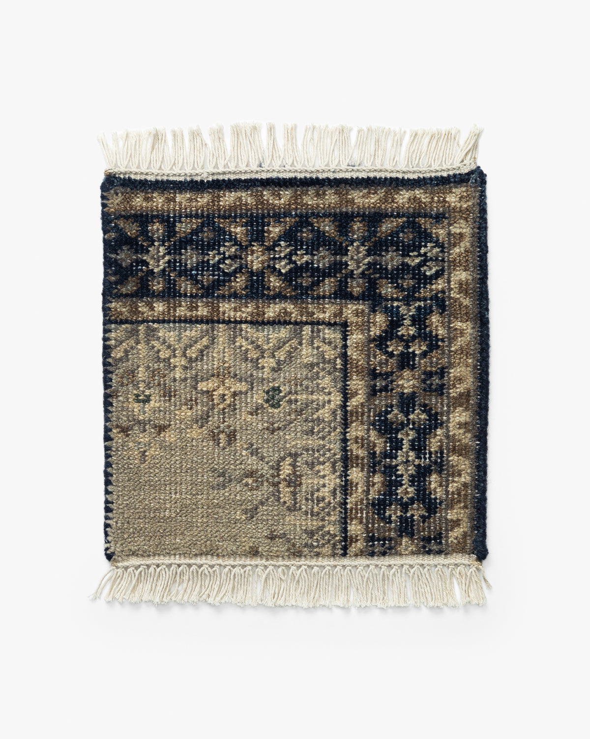 The Deveraux Hand-Knotted Wool Rug Swatch is a square, vintage-inspired sample with cream fringe and a traditional floral pattern in navy, beige, and brown. Part of the wool swatch is folded to show its reverse side, by McGee & Co.