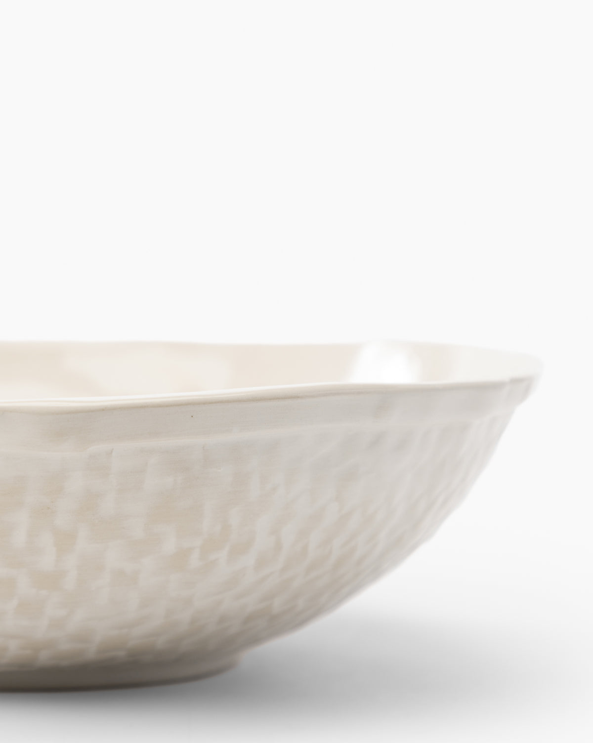 A close-up of the Dion Serving Bowl, a cream-colored ceramic piece with a woven basket design and slightly irregular rim, set against a plain white background, by Vendixs