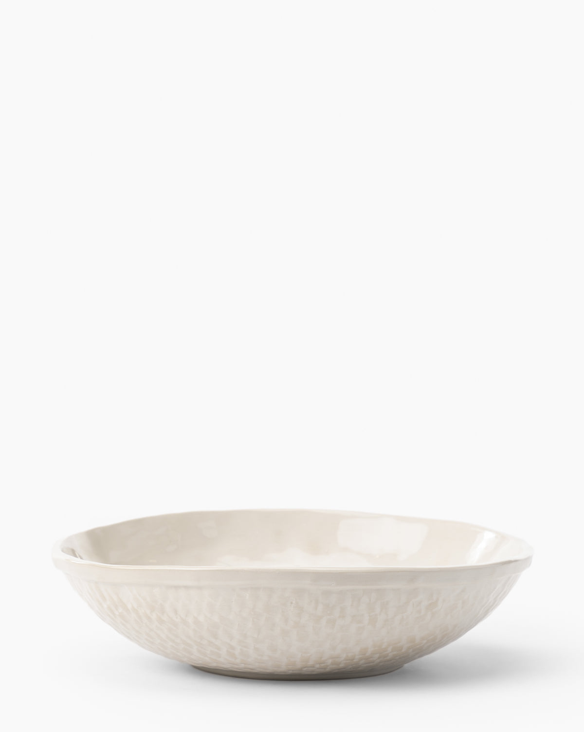The Dion Serving Bowl is a shallow, round ceramic bowl with a subtle woven basket design on the exterior and an off-white glaze, displayed against a plain white background, by Vendixs