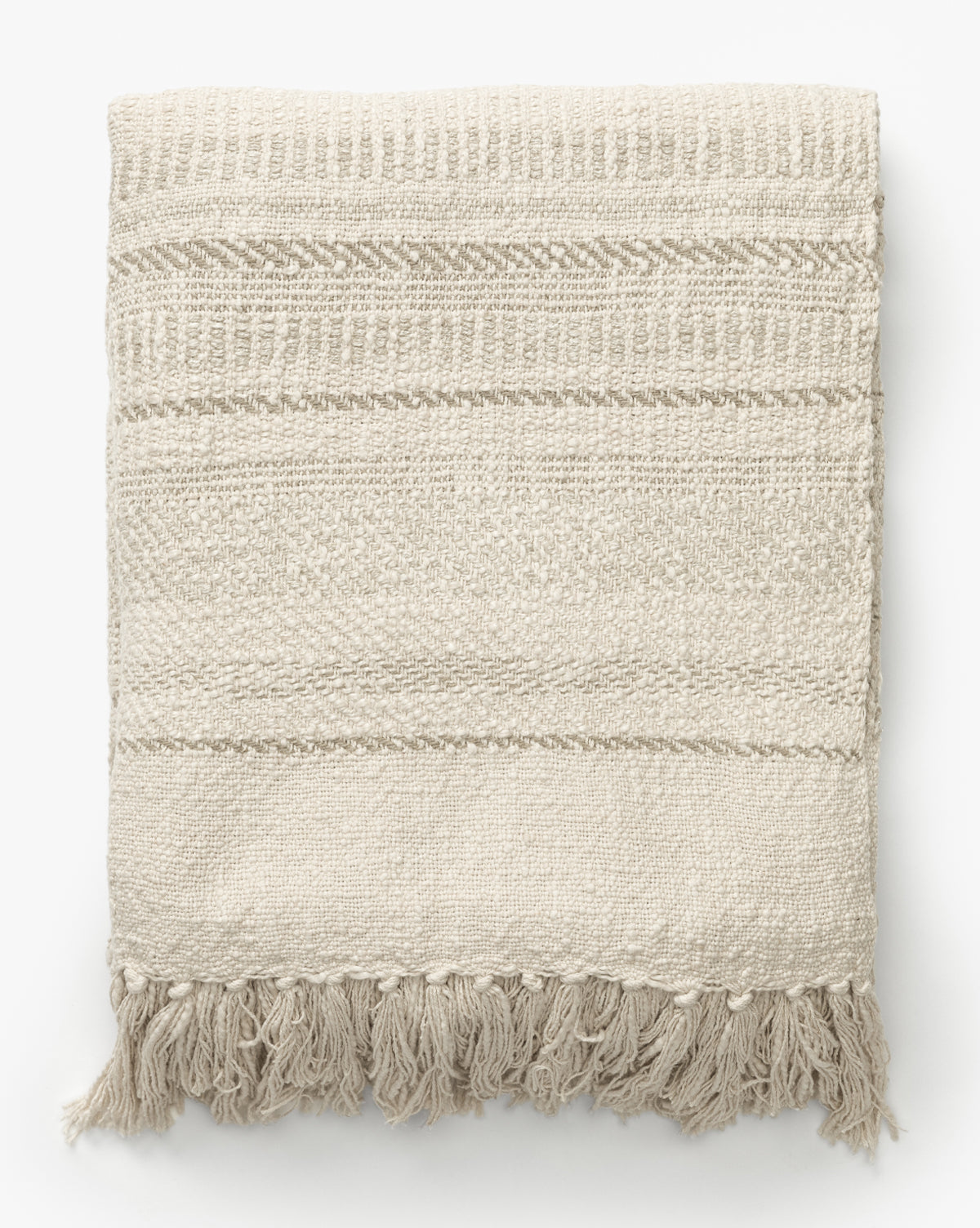 The Donahue Striped Throw by ILA HOME FASHIONS is a beige, hand-woven blanket with subtle textured patterns and fringe tassels along the bottom edge, shown folded on a white background. Vendixs