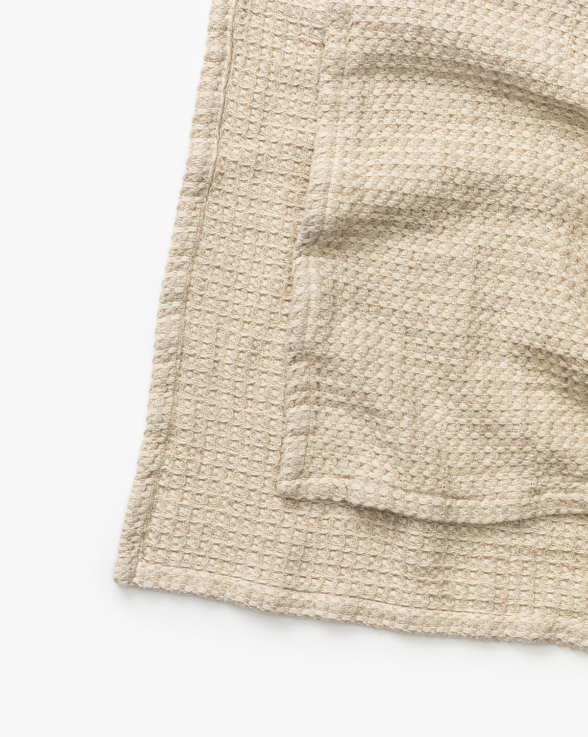 The Penedo Duffy Oversized Throw, featuring a beige textured waffle-knit cotton-hemp blend, is folded on a white surface with only part of the throw visible in the image. Vendixs