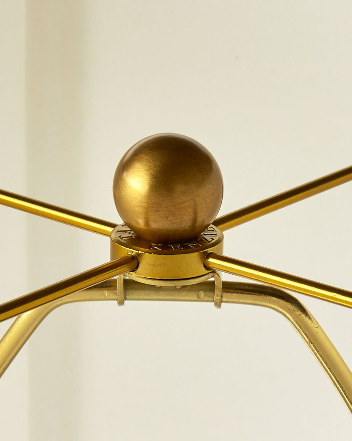 Close-up of the Dynasty Table Lamp’s metallic gold harp with a round finial on top, set against a plain background. The harp arms extend outward from the lamp’s central fixture, by Vendixs