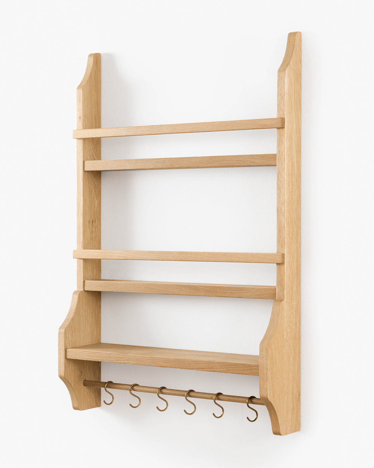 The Edna Kitchen Shelf is a wooden, wall-mounted unit with three open shelves, a lower ledge, and five metal hooks. Its heritage oak finish and angled side supports create timeless charm for your kitchen, by Vendixs