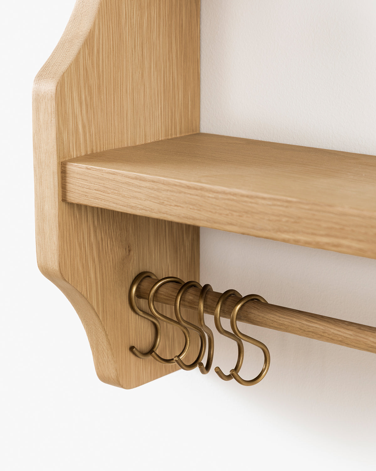 Close-up of the Edna Kitchen Shelf in heritage oak with a smooth finish, featuring a horizontal rod and brass S-hooks. This open shelving unit is mounted on a white wall, by Vendixs