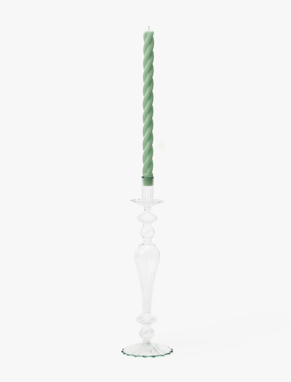 A tall, clear glass taper holder with a decorative design holds a light green twisted candle against a plain white background, resembling the Vendixs x Loeffler Randall Effie Taper Holder by McGee & Co.
