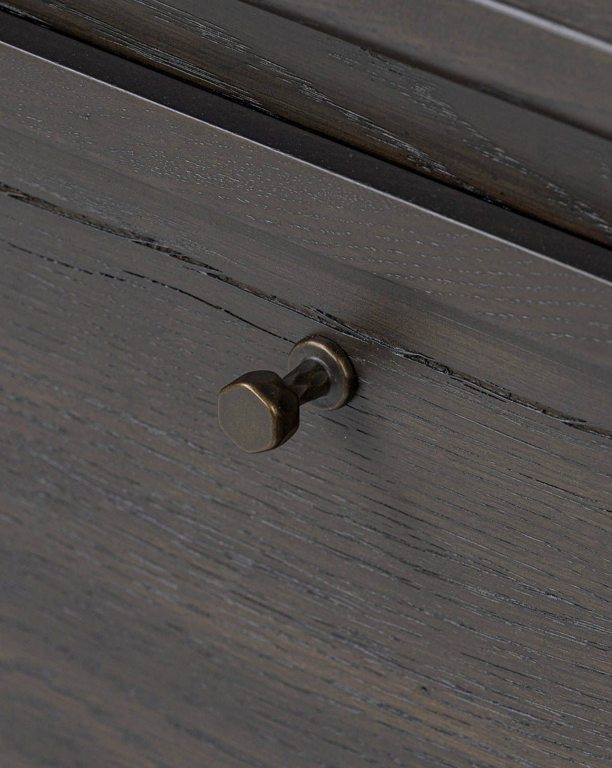 Close-up of the Eldoria Oak Sideboard drawer front, featuring dark wood grain and a small round antique brass knob. Its textured finish enhances the rustic charm and modern deco style of this elegant furniture piece, by Vendixs