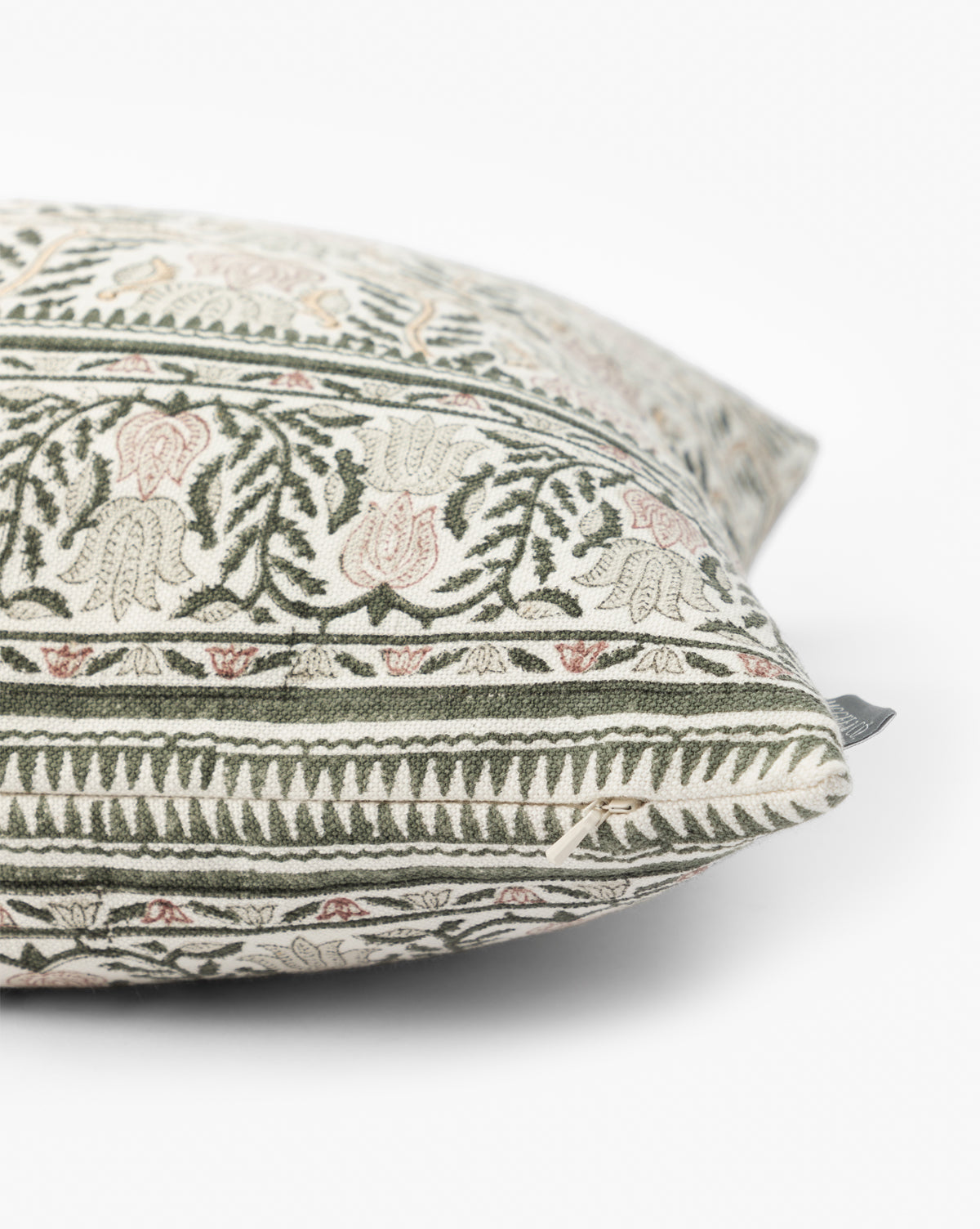 A close-up of the Ellsbeth Pillow Cover reveals a detailed green and light pink floral-geometric pattern on cream cotton-linen, highlighting its fabric texture, fine stitching, small tag, and artisanal quality, by Vendixs