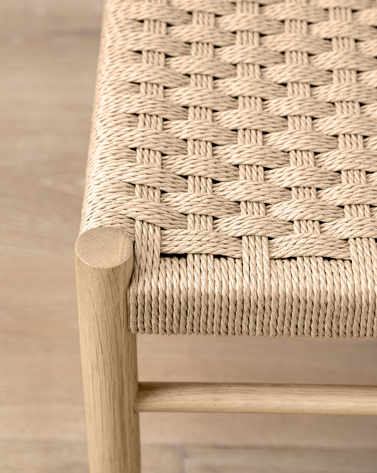 Close-up of the Eloise Woven Counter Stool, featuring a light wood frame and tightly interlaced natural fiber seat that highlights its authentic Danish design, set against a wooden floor background by McGee & Co.