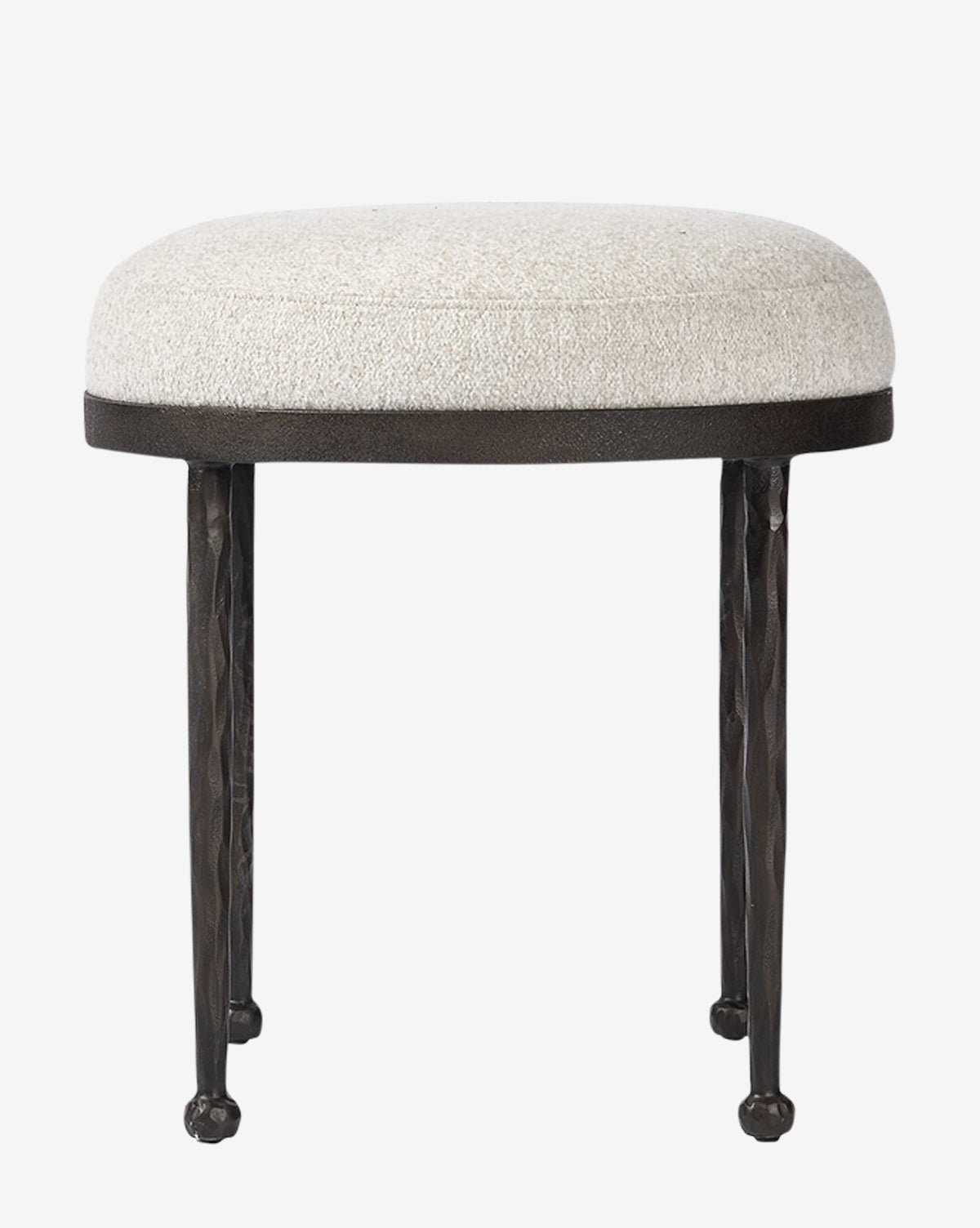 The Emmett Stool by Four Hands features a small, round design with a light beige upholstered cushion and three textured black metal legs, making it an ideal accent piece against a plain white background. Vendixs