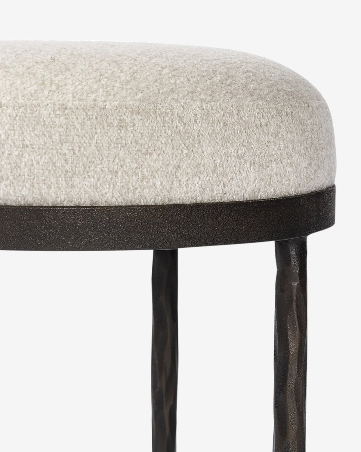 Certainly! Here’s your blended sentence: The Emmett Stool by Four Hands features a round hammered bronze base, textured light beige upholstered seat, dark metal rim, and two black hammered metal legs—an ideal accent piece against a white background by Vendixs