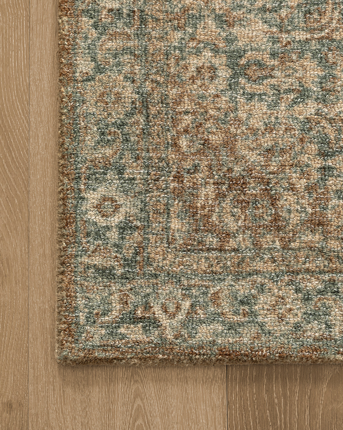 A close-up of the Endicott Hand-Tufted Wool Rug showcases its ornate, traditional design in beige, brown, and blue tones, lying on a light wooden floor, by Vendixs