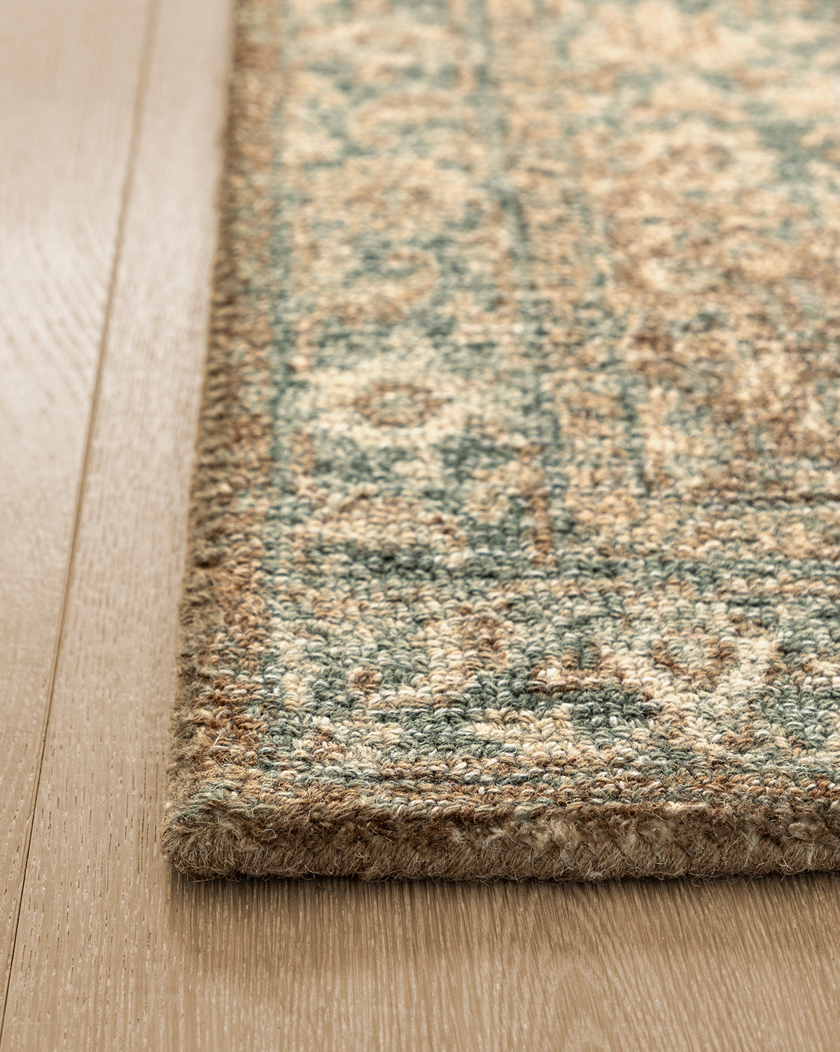 A close-up of the corner of the Endicott Hand-Tufted Wool Rug, featuring a blue and beige geometric pattern, placed on a light wood floor, by Vendixs