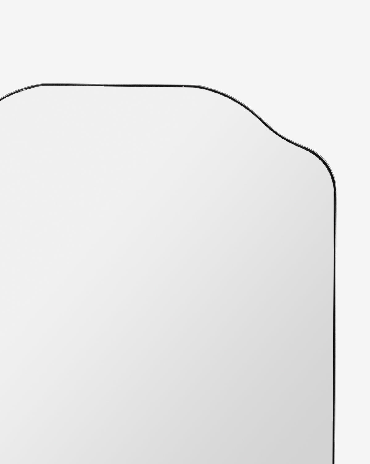 A close-up of the Ethel Wall Mirror’s upper section, featuring a metal frame with curved top corners, set against a plain white background, by Vendixs