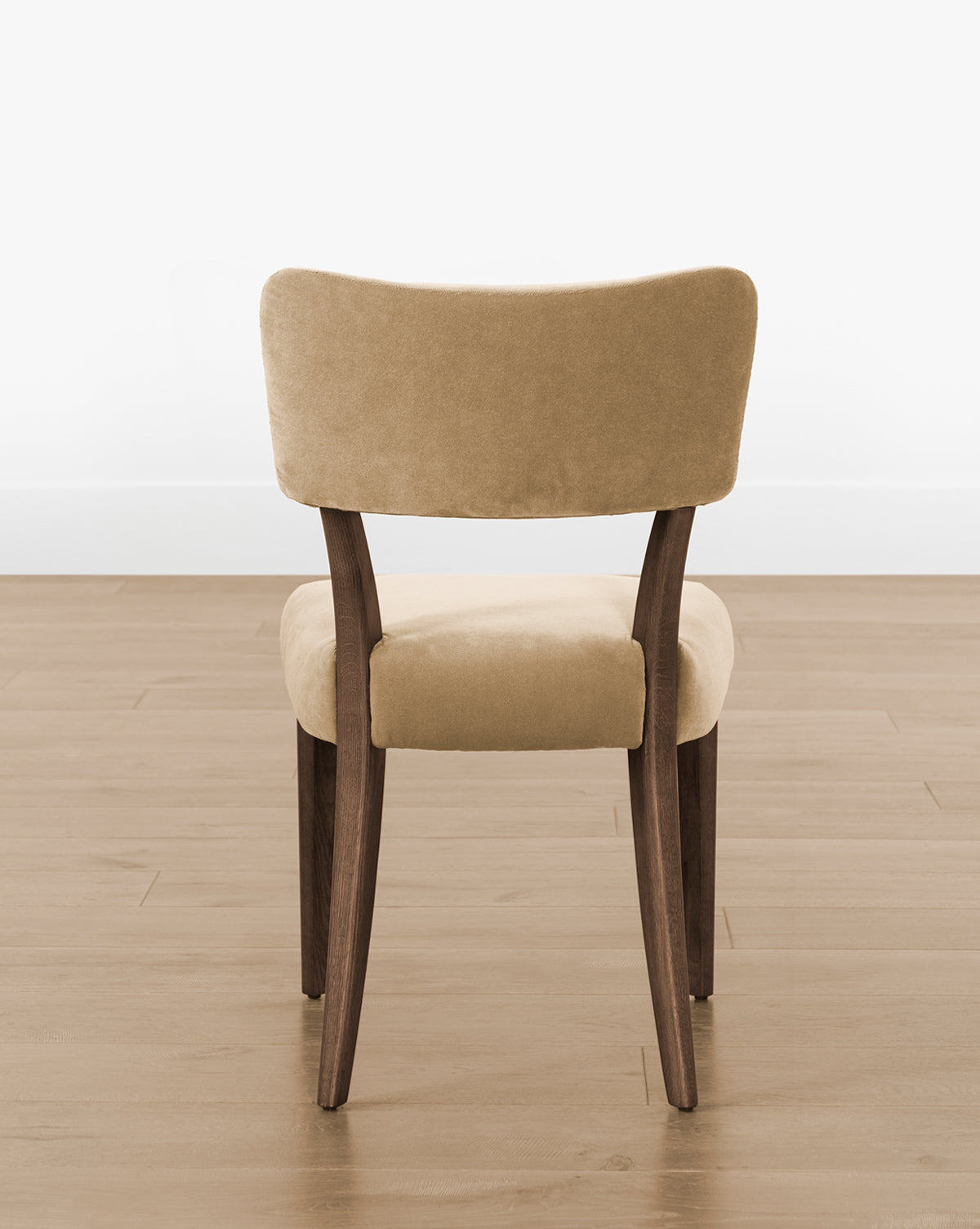The Etienne Dining Chair (Ready to Ship) has a beige upholstered seat and backrest, curved wooden legs, and frame, offering a modern vintage style—perfect for light wood floors and plain white walls, by Vendixs