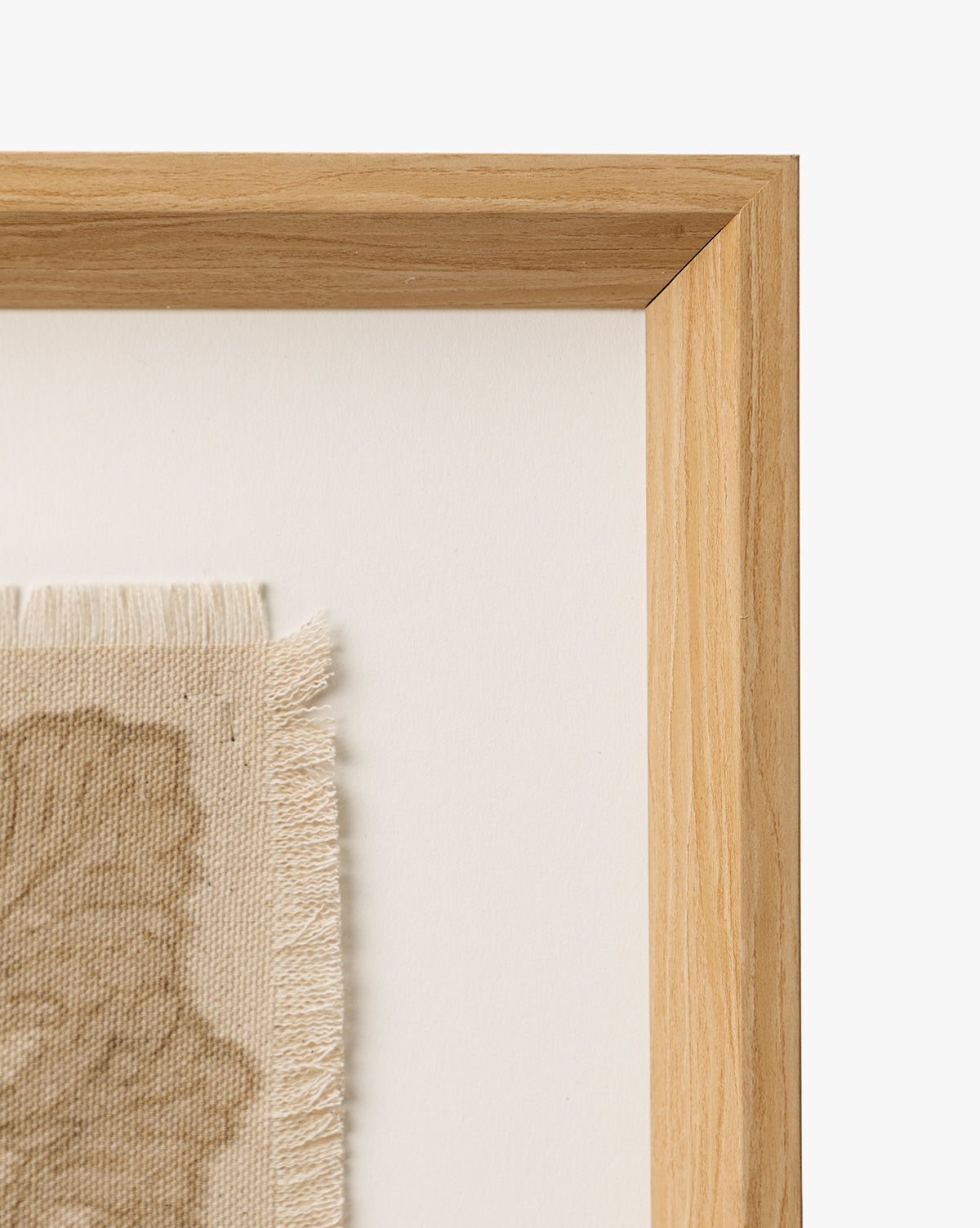 A close-up of the European Flare frame’s natural woodgrain corner surrounds vintage-style wall art—beige fabric with frayed edges and a subtle leaf design—displayed on a white background, by Vendixs