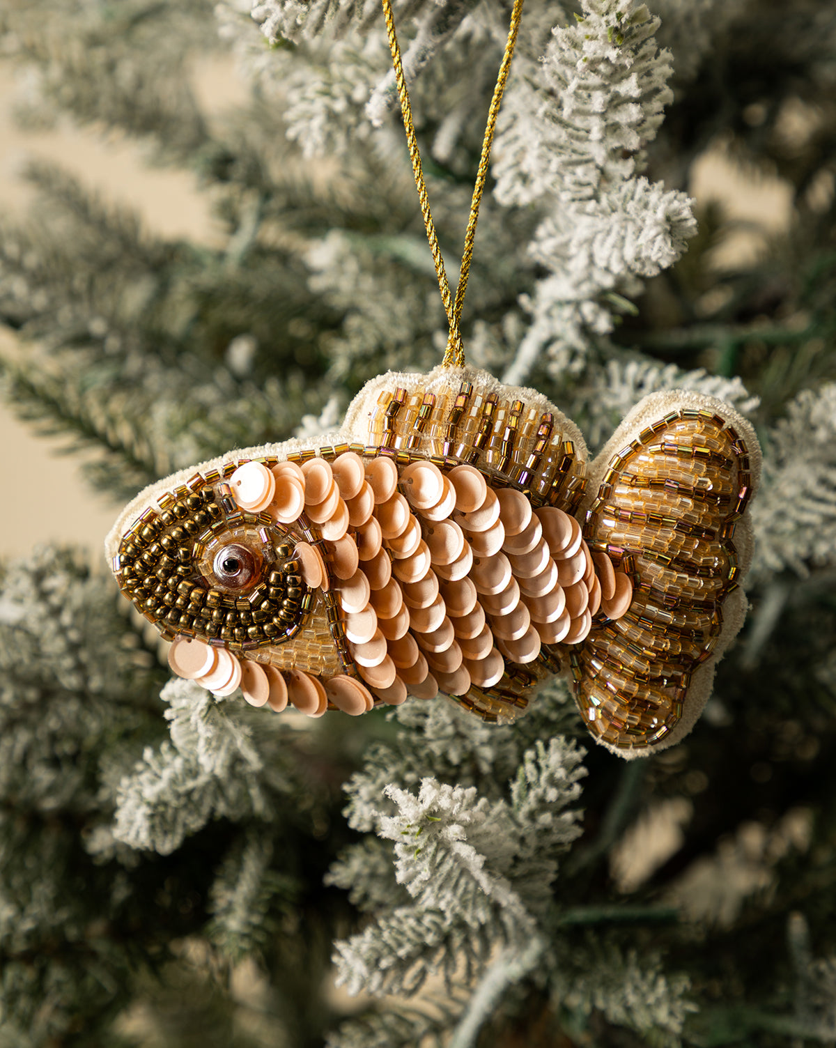 Fabric Sequin Fish Ornaments (Set of 2), adorned with hand-applied beads, hang from a snowy artificial Christmas tree branch—a charming addition to your holiday décor, by Vendixs