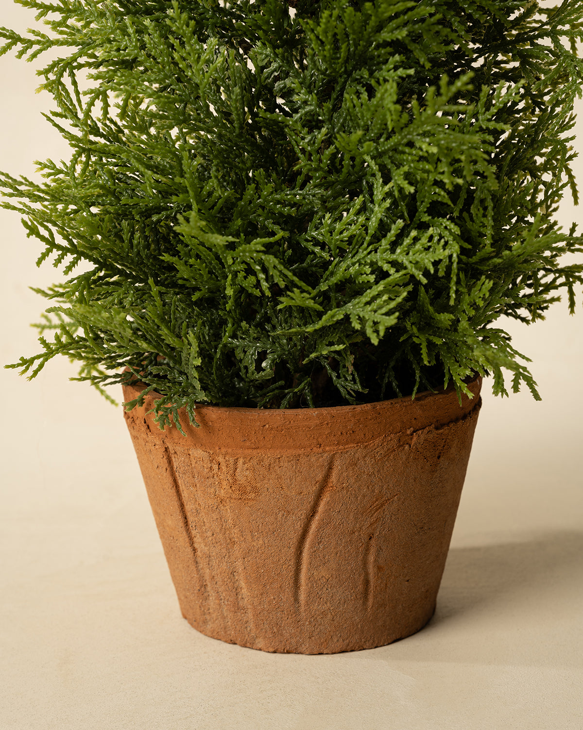 A close-up of the 17" Cypress Faux Potted Tree featuring lush green foliage in a textured brown terracotta pot, set against a plain, light background, by Vendixs