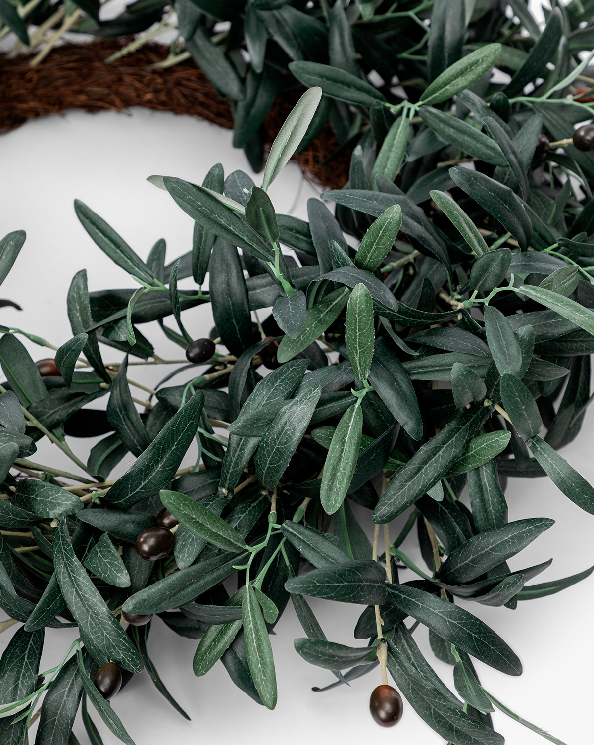 A close-up of the Faux Olive Berry Wreath featuring dark green, realistic foliage and small black olives, displayed against a white background, by Vendixs