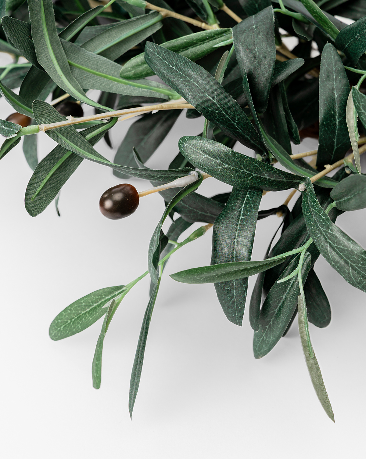 A close-up of the Faux Olive Berry Wreath showcases slender green leaves and dark olives, capturing a lifelike greenery look against a white background, by Vendixs