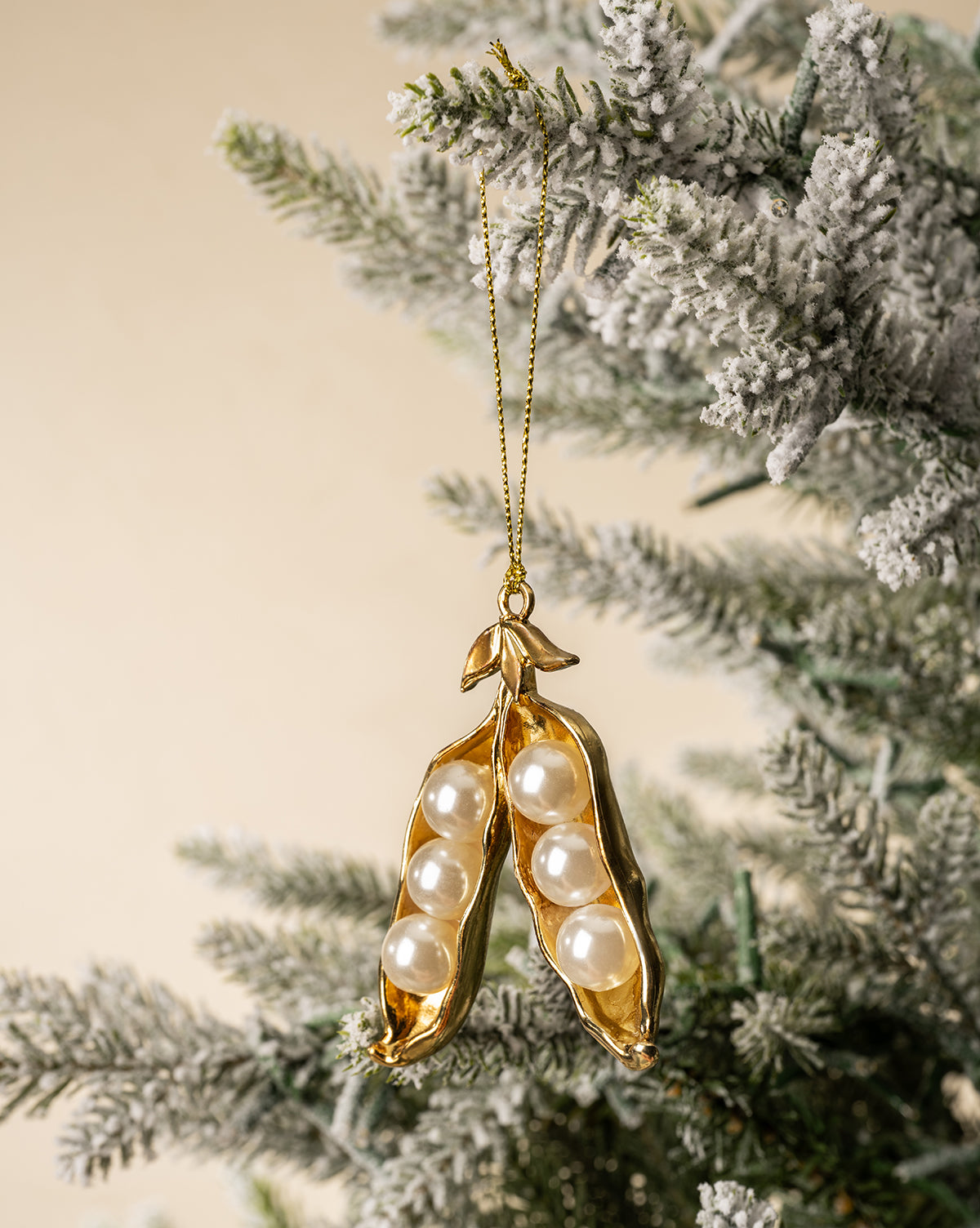 The Faux Pearl Pea Pod Ornament, featuring five pearl-like beads, hangs from a snow-dusted Christmas tree branch to bring festive elegance to your holiday decor, by Vendixs