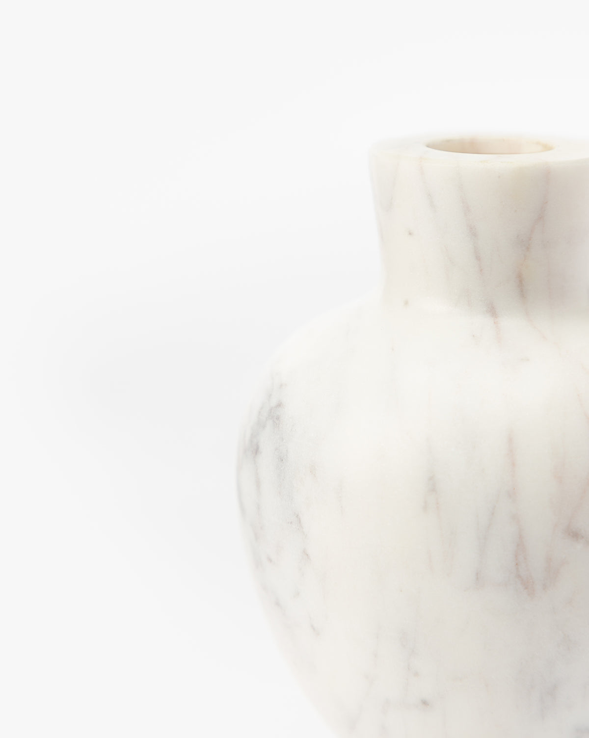 A close-up of the Fera Bud Vase, featuring white marble with subtle grey veining. This elegant vase’s rounded body and narrow neck are partially visible against a plain white background, by Vendixs