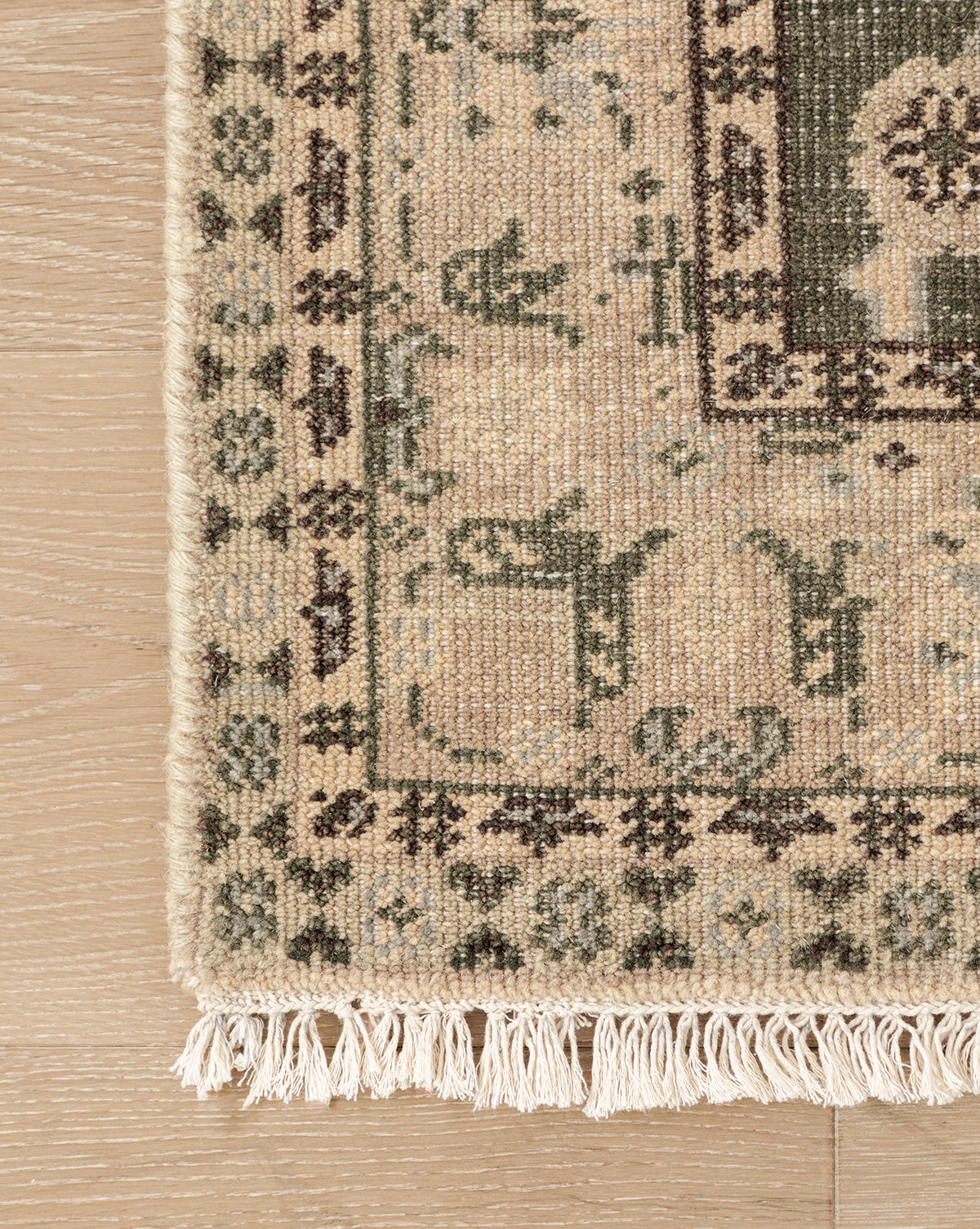 A close-up of the Fernwood Hand-Knotted Wool Rug shows its intricate beige, green, and pink motifs on a light wooden floor, with delicate white fringes lining the edge, by Vendixs