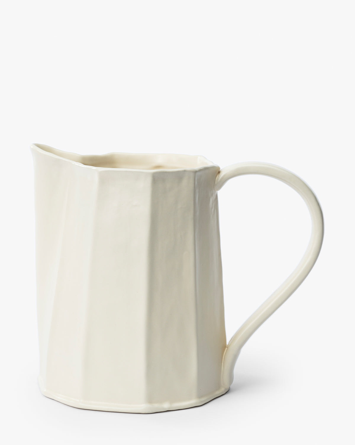 The Fielding Ceramic Pitcher features a cream-colored stoneware body with a faceted, angular surface and a large curved handle, making it ideal for rustic kitchen decor, by Vendixs Shown against a plain white background.