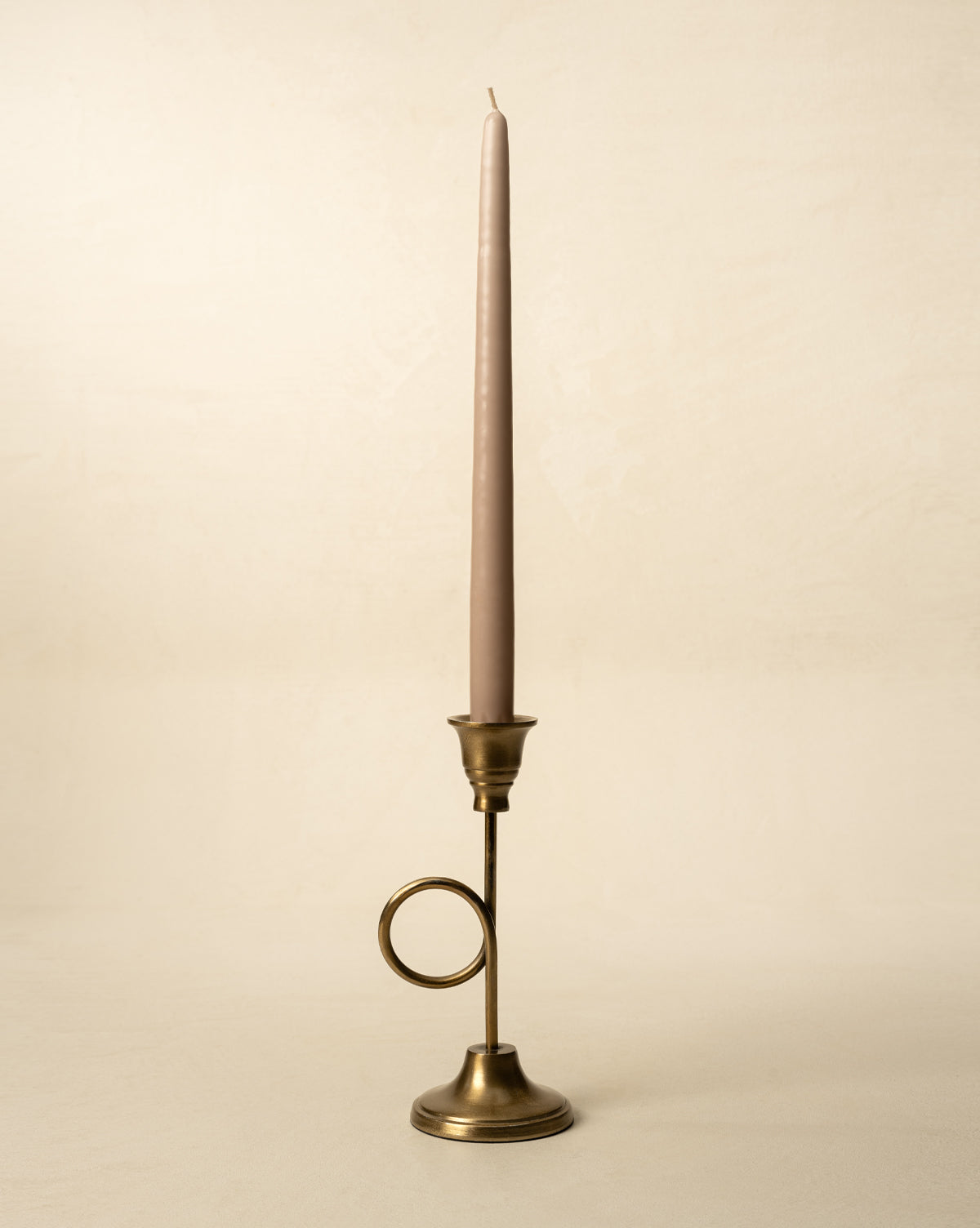 A tall, slender mauve taper candle sits in the French Horn Taper Holder with a circular handle, set against a neutral beige background—ideal for elegant holiday styling, by Vendixs