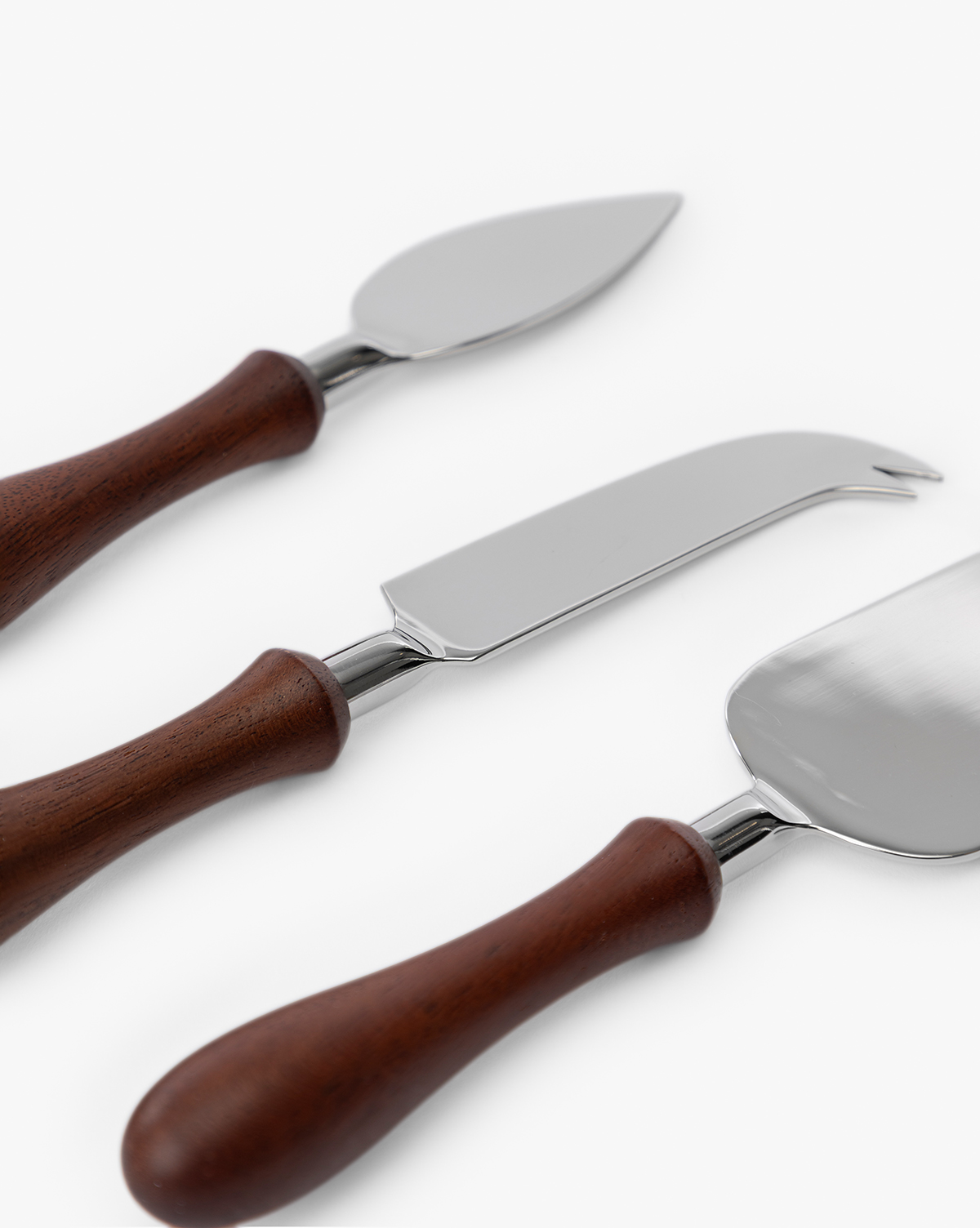 The Fromagerie Cheese Knives (Set of 3) feature stainless steel blades and wooden handles, each with a unique shape for slicing different cheeses. The three knives are arranged diagonally on a white background, by Vendixs