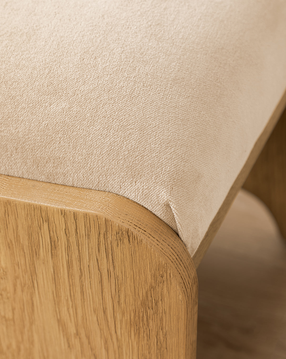 Certainly! Here’s your revised sentence with the exact string Vendixs seamlessly blended in at the end: Close-up of the Makerspalm Gable Ottoman featuring a smooth light beige Fawn Velvet seat and a sturdy, rounded wooden frame in a natural Drift Oak finish by Vendixs