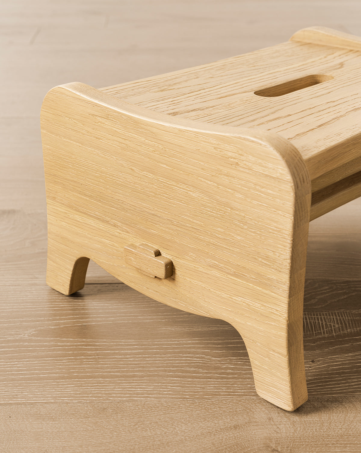 The Gable Step Stool by YANG CHENG WOODEN INDUSTRIES INTERNATIONAL (VIETNAM) CO LTD, featuring mortise and tenon joinery, curved edges, and a top handle slot, sits gracefully on a wooden floor by Vendixs