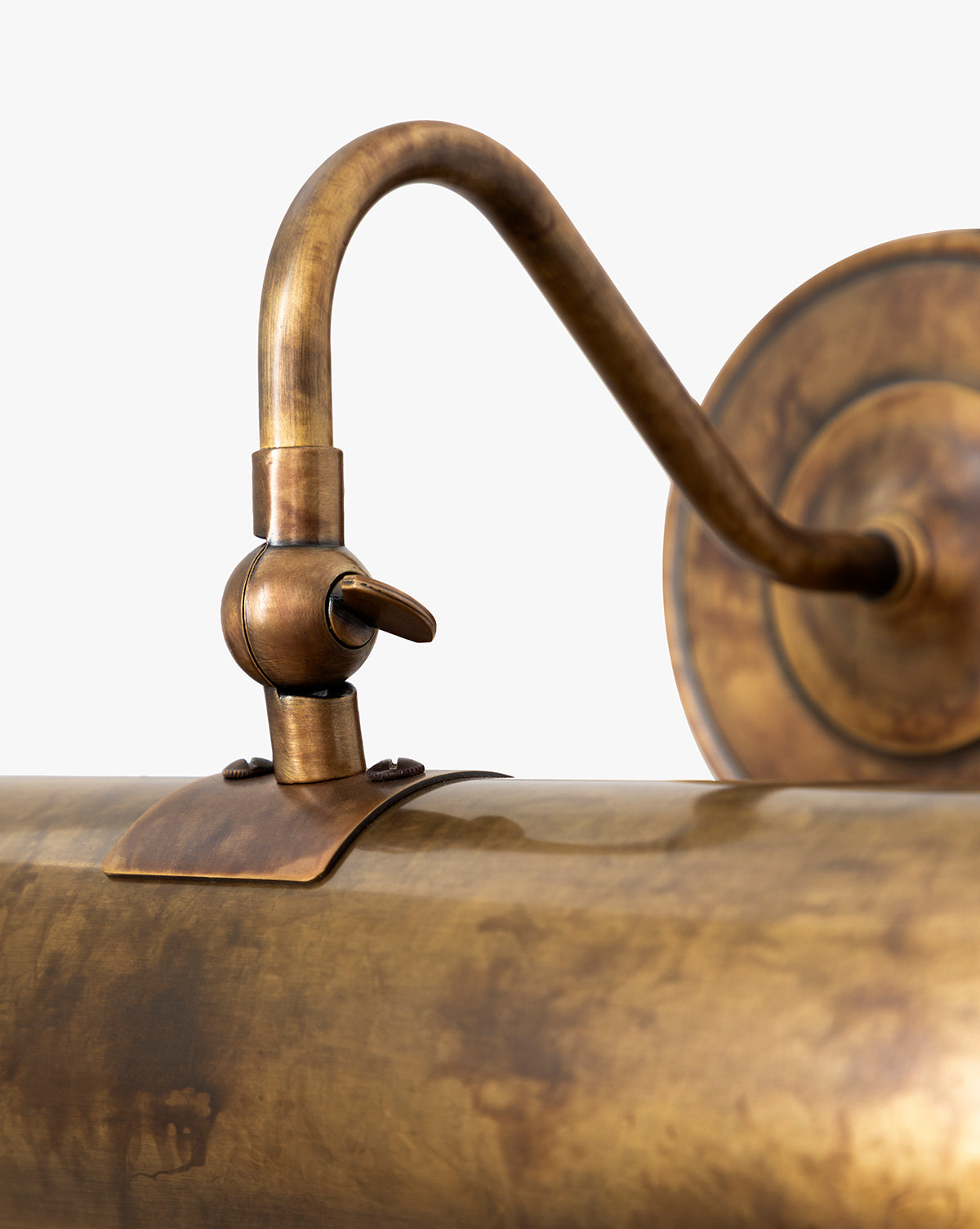 Close-up of the Gallery Picture Sconce in burnished bronze, featuring a curved arm, cylindrical shade, weathered patina finish, and detailed metalwork set against a plain background, by Vendixs