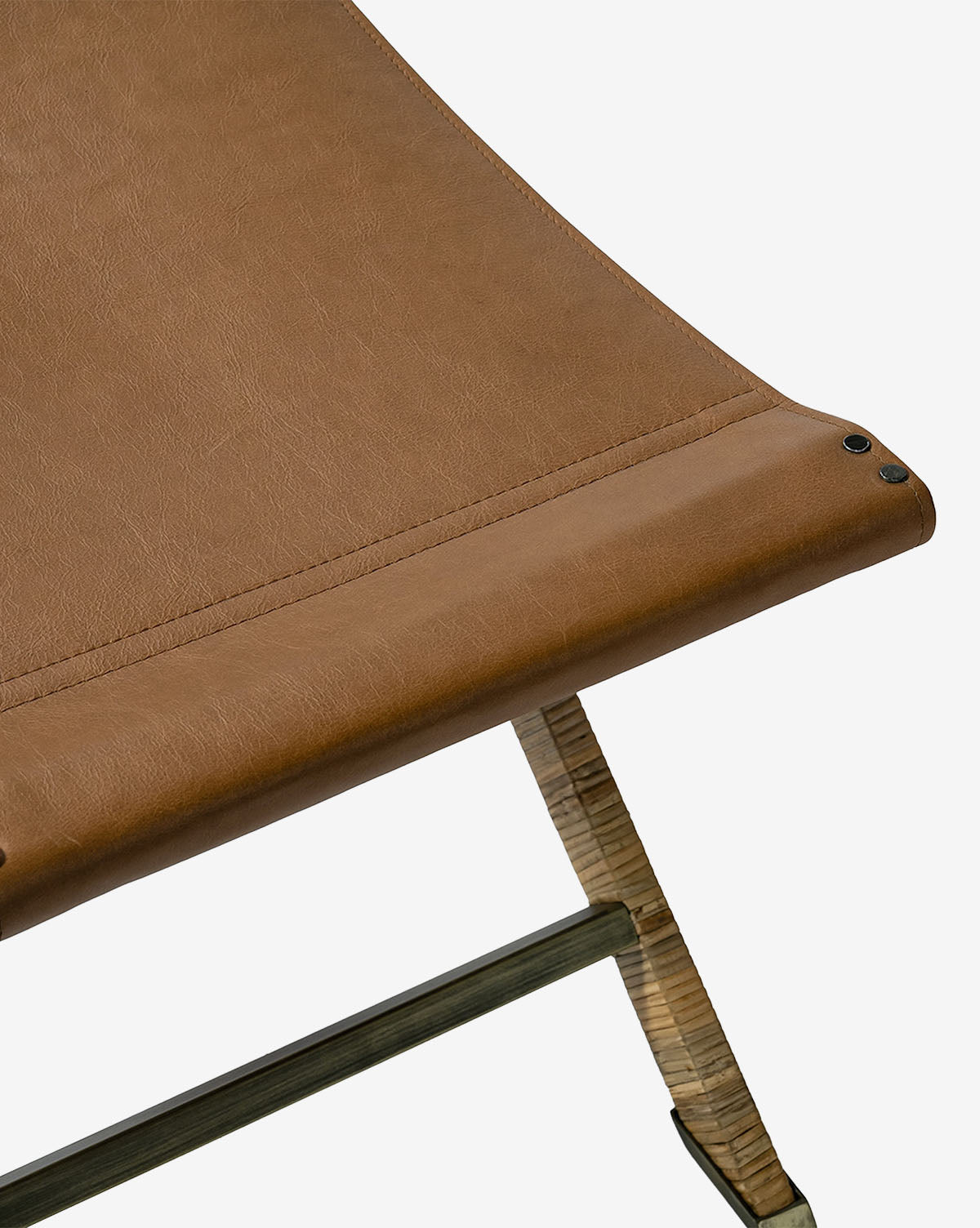 Close-up of the Palecek Gertie Stool featuring a brown leather seat, wooden legs, visible stitching, and three black rivets at the corner, shown against a white background. Vendixs